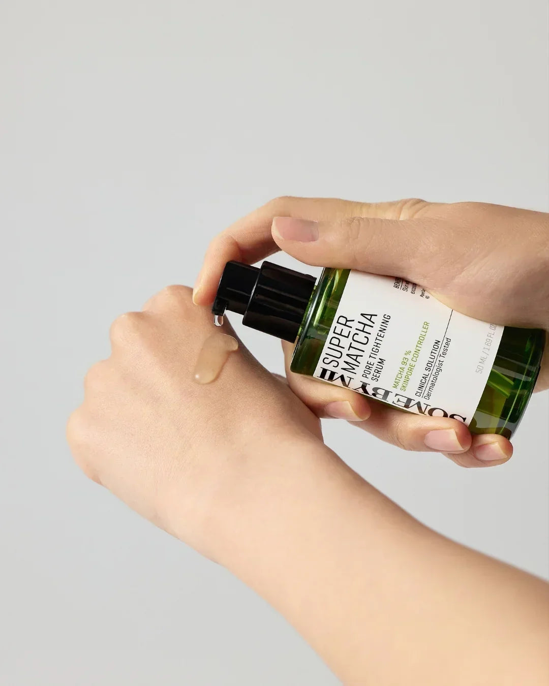 Hand dispensing Super Matcha Pore Tightening Serum from green bottle onto back of other hand