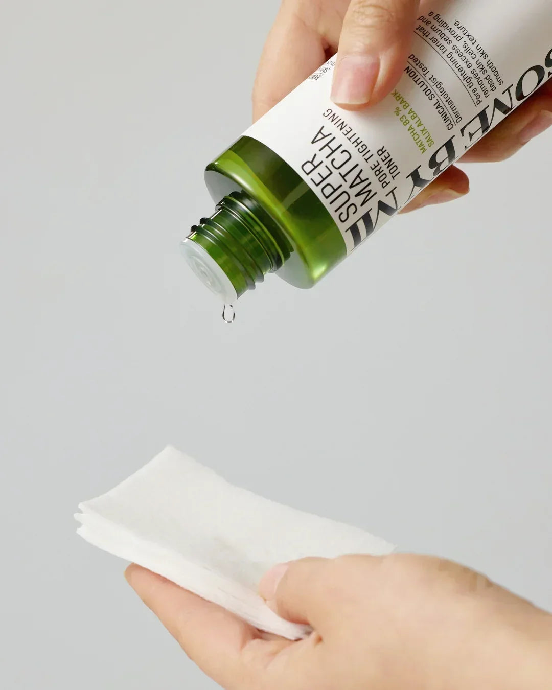 Droplet of Super Matcha Pore Tightening Toner falling from green bottle onto cotton pad