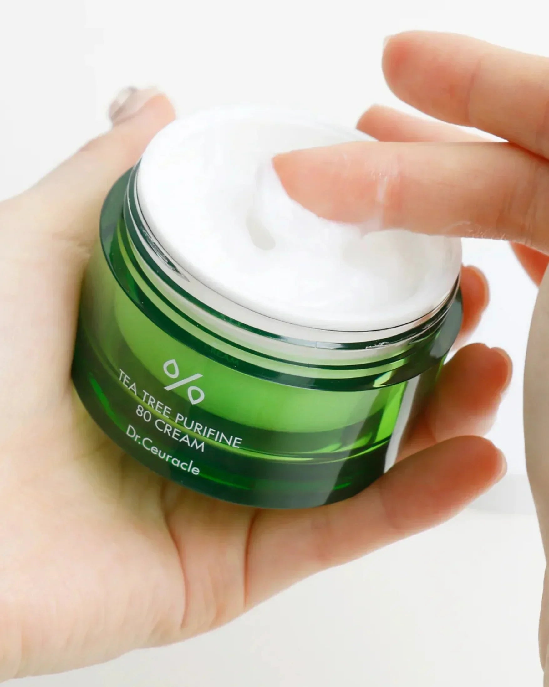 Hand holding green jar of Dr. Ceuracle Tea Tree Purifine 80 Cream with finger dipping into white cream
