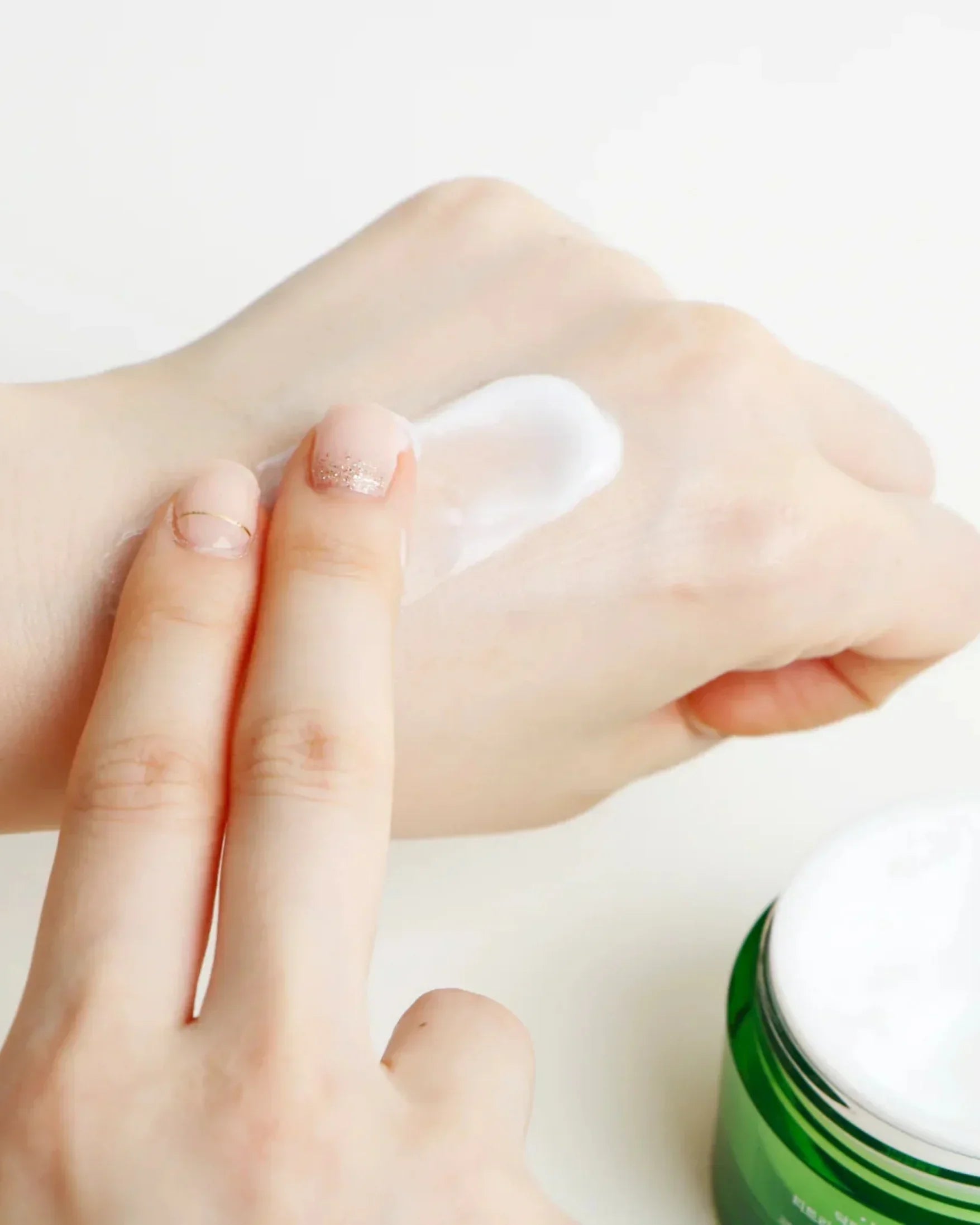 Person applying white tea tree purifying cream on hand with green cream jar nearby
