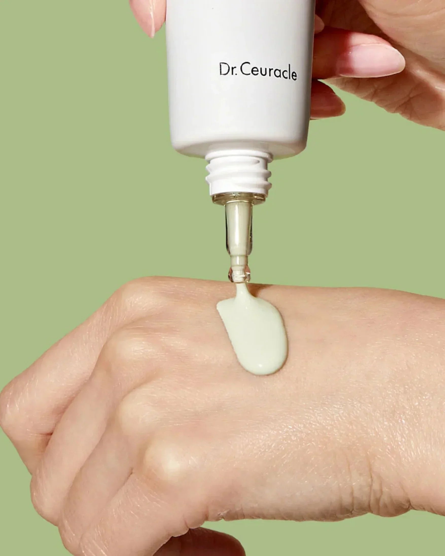 Dr. Ceuracle skincare cream being dispensed onto hand against green background