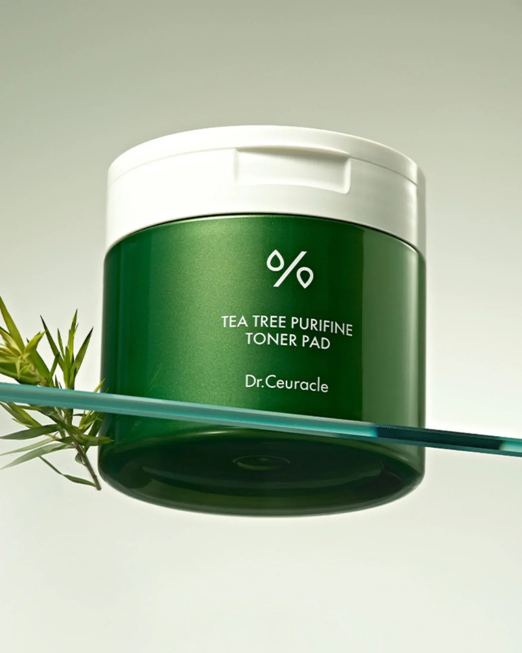 Green container of Dr.Ceuracle Tea Tree Purifine Toner Pad with white lid and tea tree branch