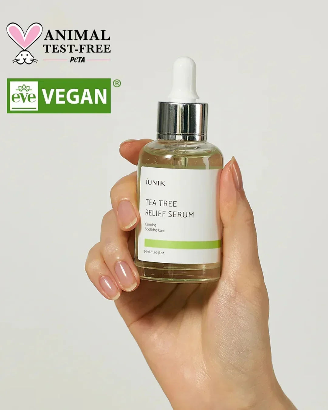 Hand holding iUNIK Tea Tree Relief Serum bottle with dropper, vegan and animal test-free logos