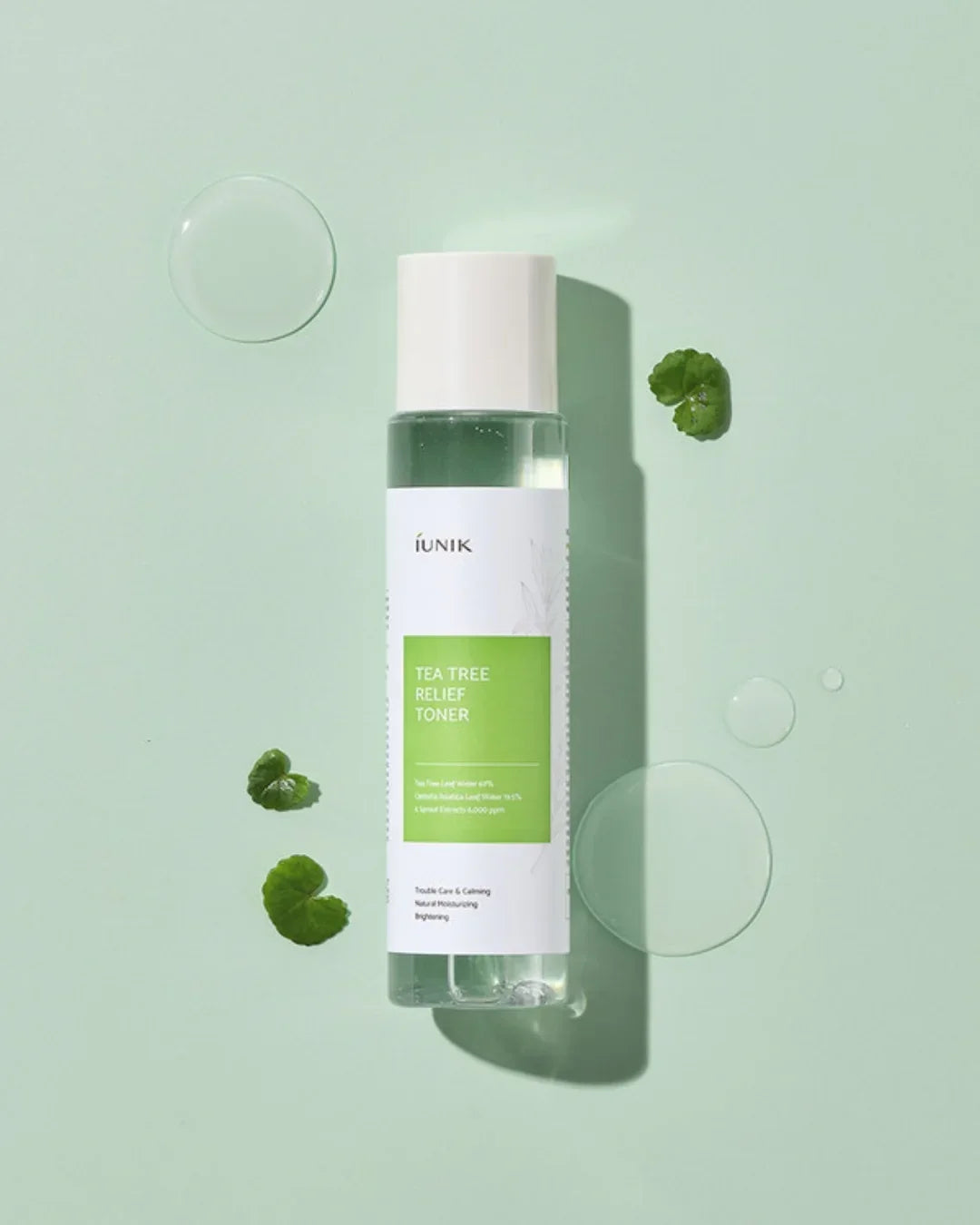iUNIK Tea Tree Relief Toner bottle with green label on light green background with water droplets and green leaves