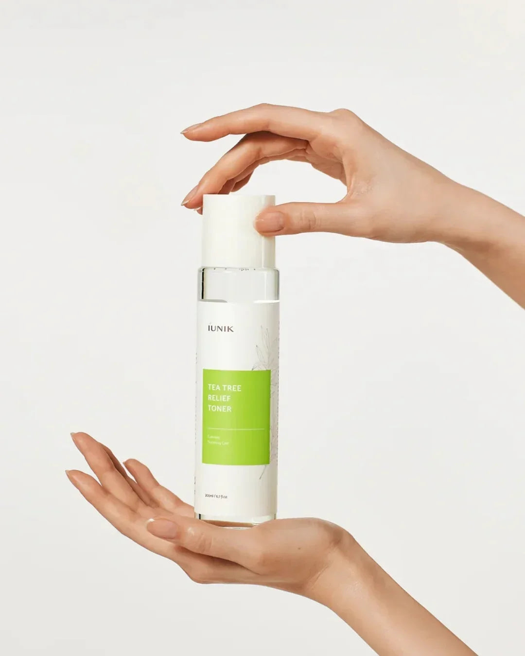 Hands holding iUNIK Tea Tree Relief Toner bottle with a white and green label on plain background