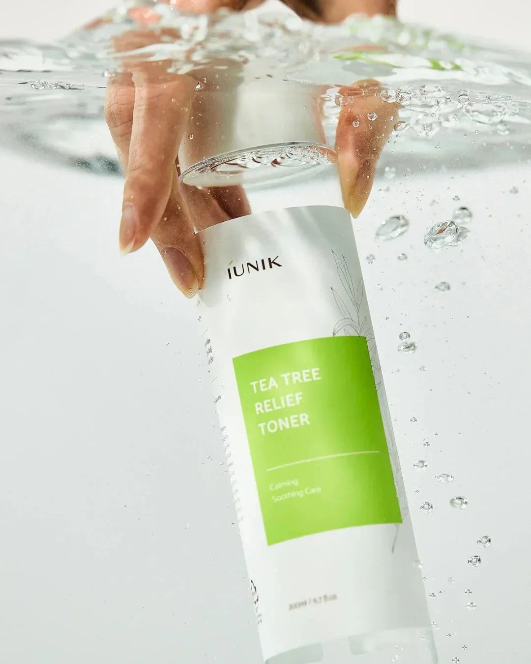 Hand holding iUNIK Tea Tree Relief Toner underwater with bubbles, skincare product focus