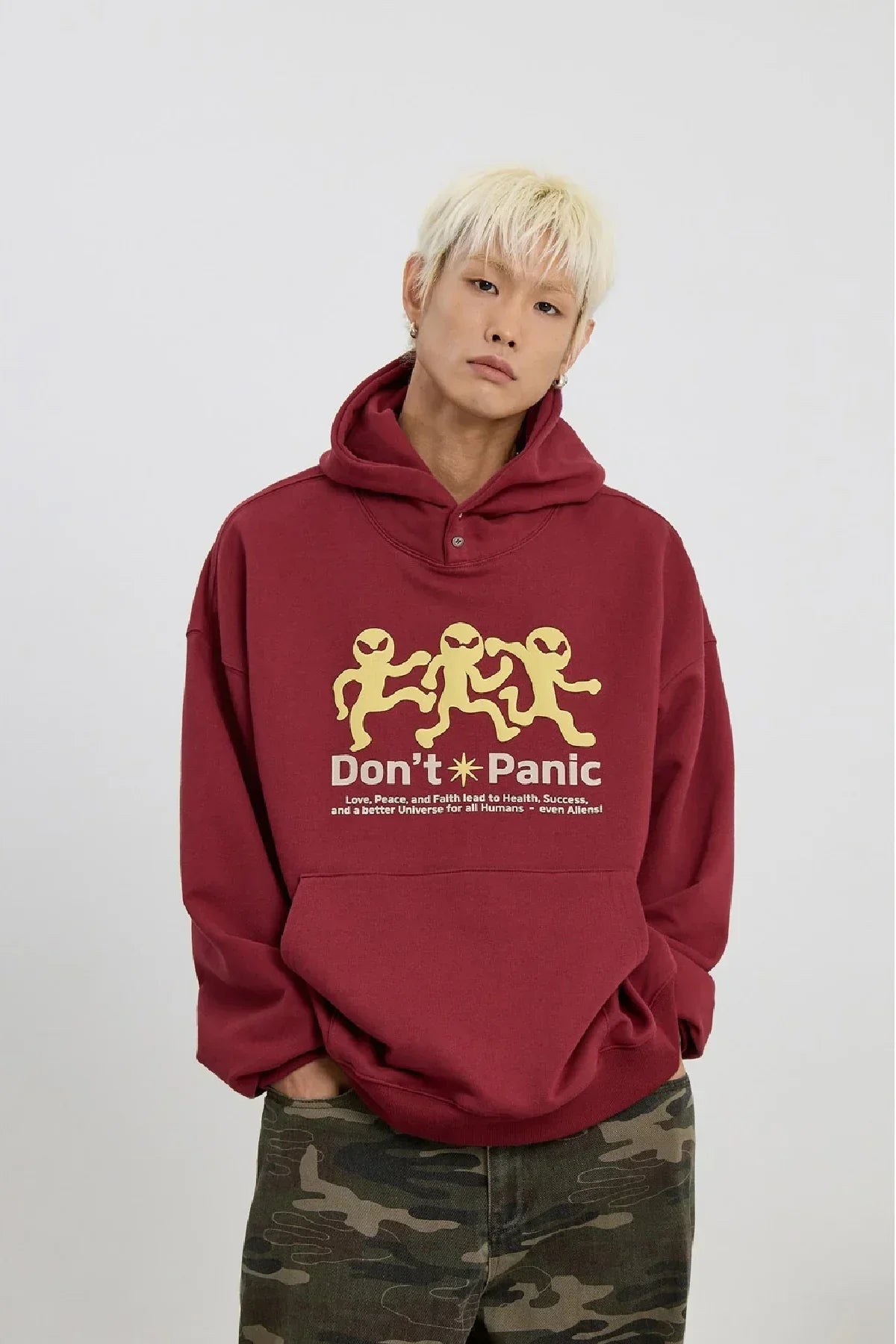 Young man wearing burgundy hoodie with three yellow alien figures and text Don't Panic on front