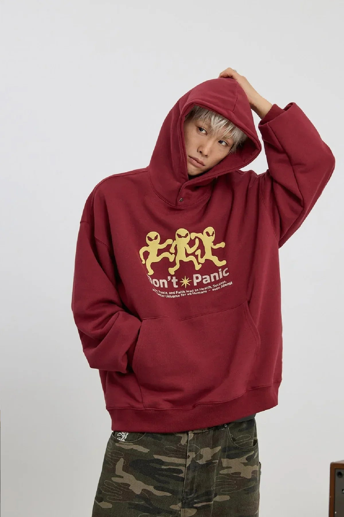 Person wearing burgundy hoodie with three yellow dancing aliens and 'Don't Panic' text, paired with camouflage pants