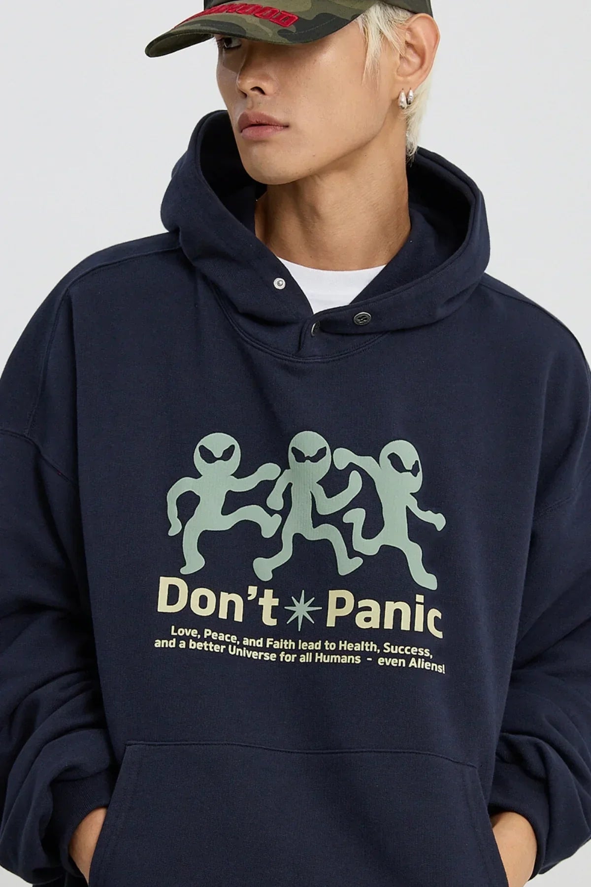 Close-up of a person wearing navy blue hoodie with three green alien figures and 'Don't Panic' text