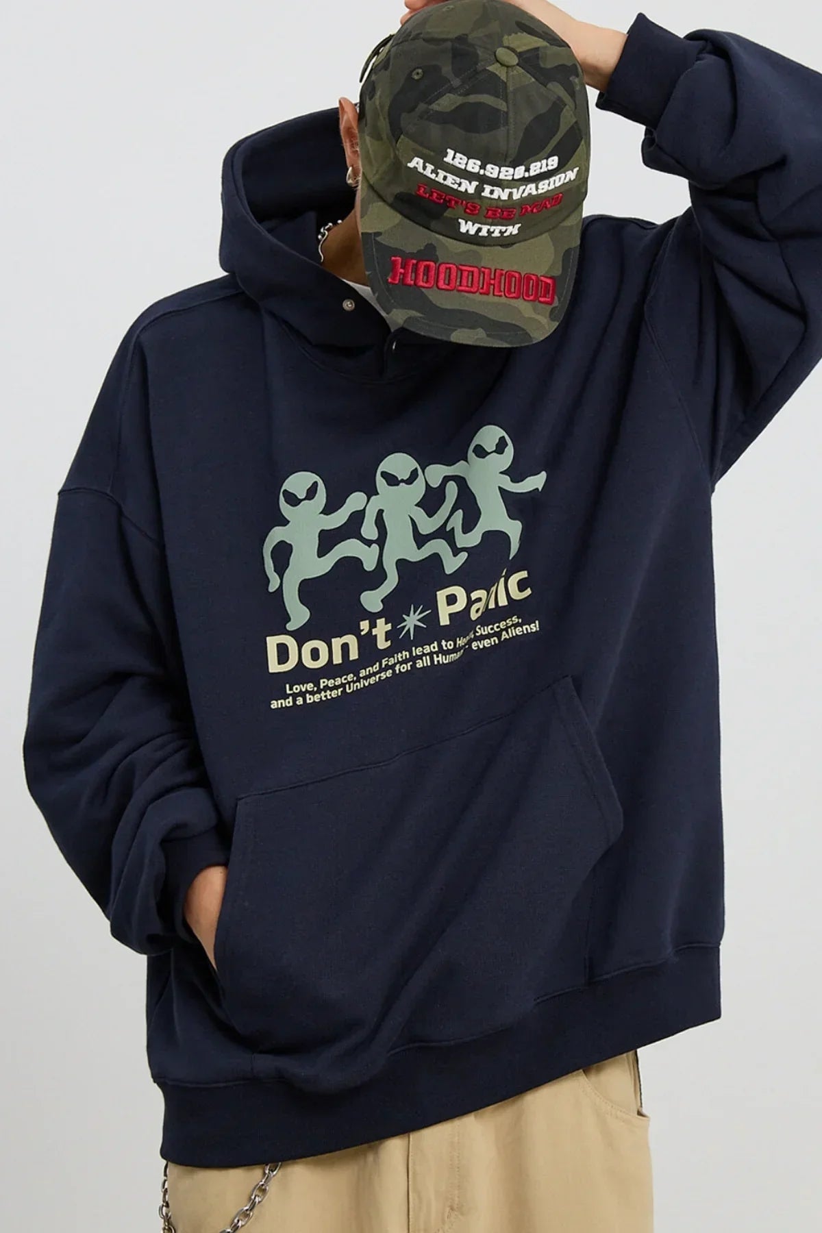 Person wearing navy hoodie with dancing alien graphics and text "Don't Panic," paired with camo cap featuring "Alien Invasion" and "HOODHOOD" embroidery.