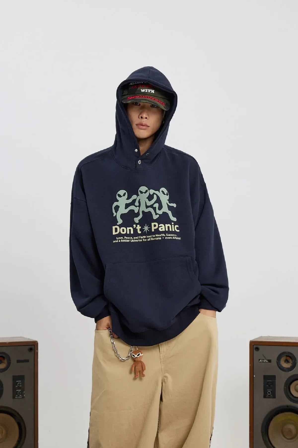 Person wearing navy hoodie with dancing alien graphic and Don't Panic text, beige pants, and cap