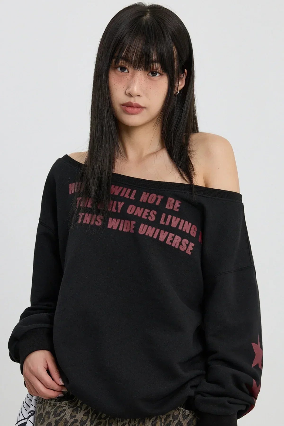 Young woman with long black hair wearing off-shoulder black sweatshirt with red text and star design