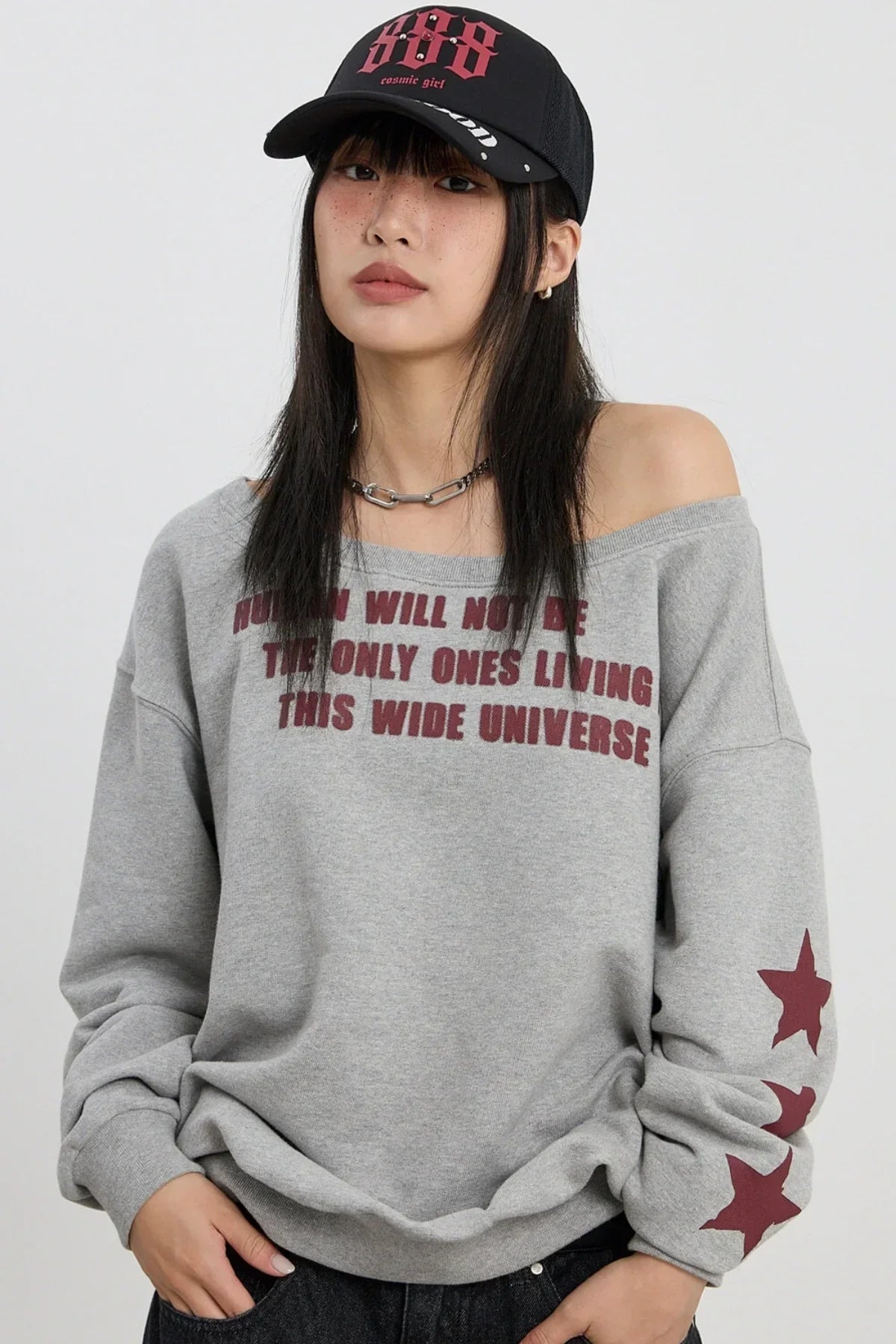 Woman wearing off-shoulder grey sweatshirt with red star lettering and black cap