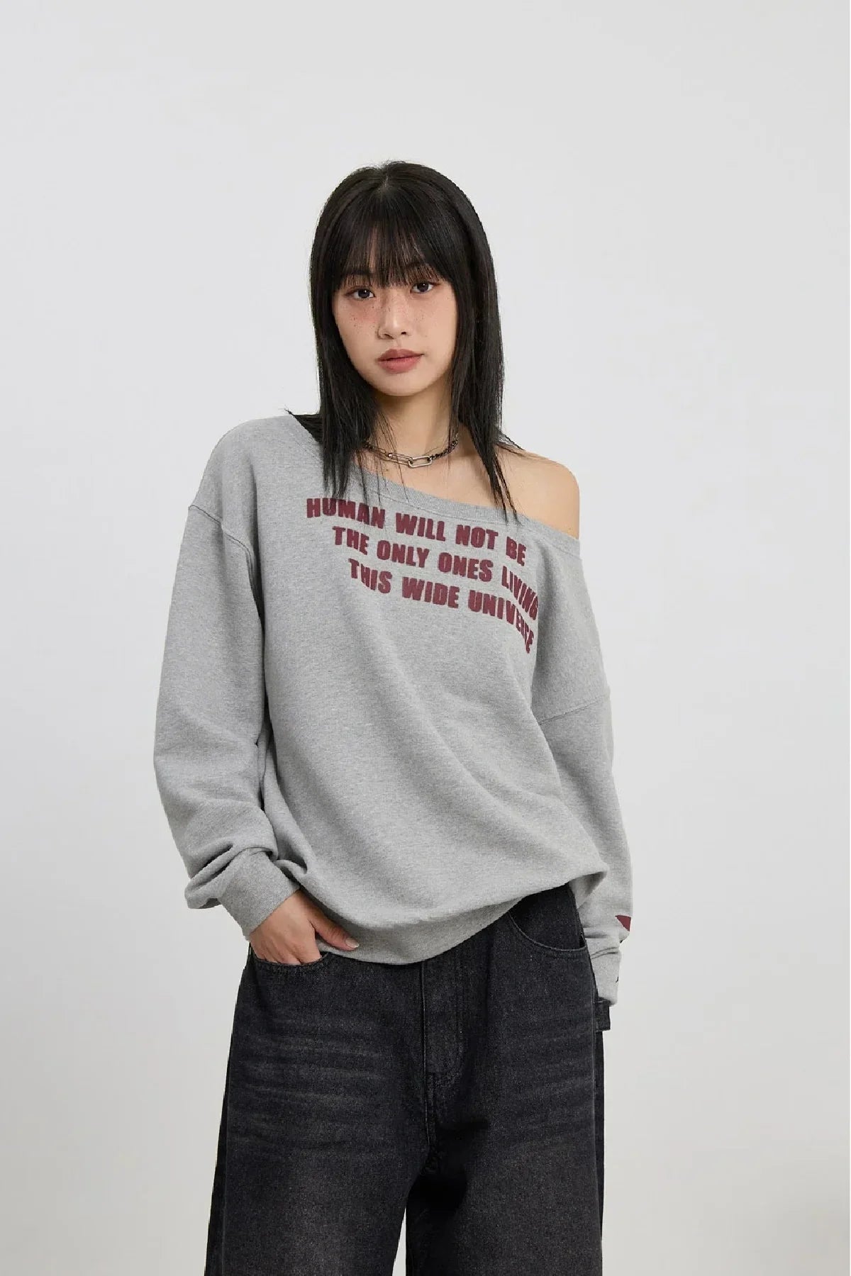 Woman wearing grey off-shoulder sweatshirt with red text and black wide-leg jeans