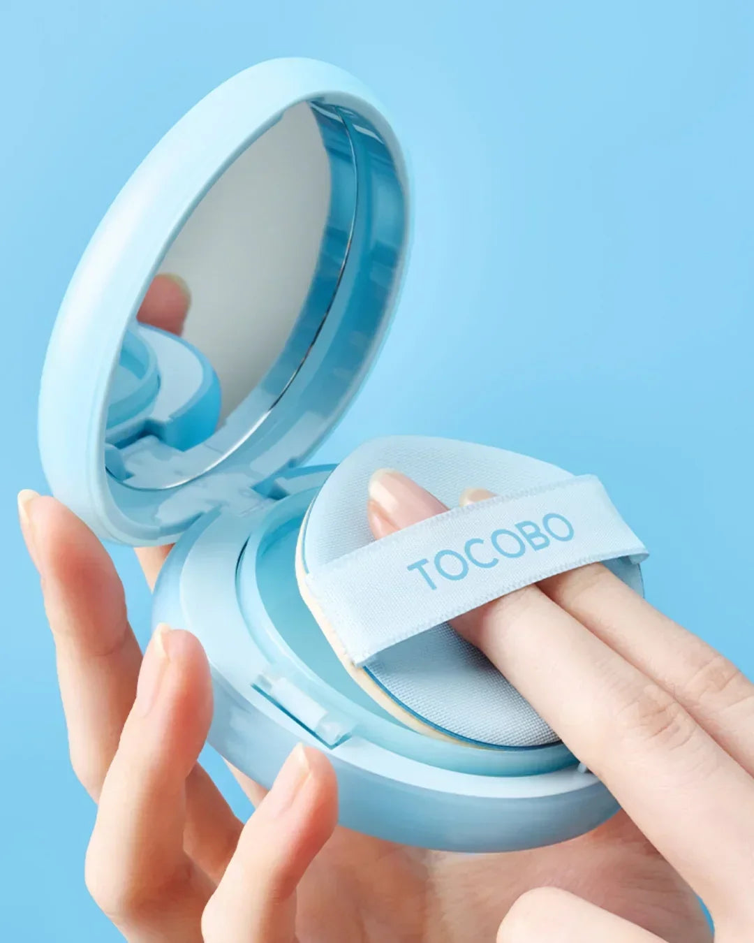 Hand holding open blue TOCOBO sun cushion compact with mirror and makeup puff