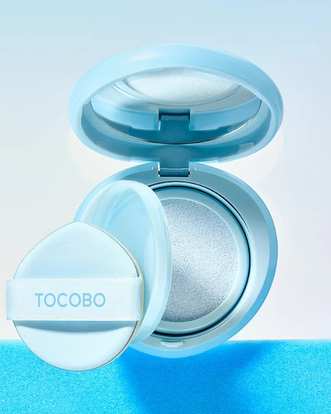 Open blue TOCOBO cushion compact with puff applicator on blue surface