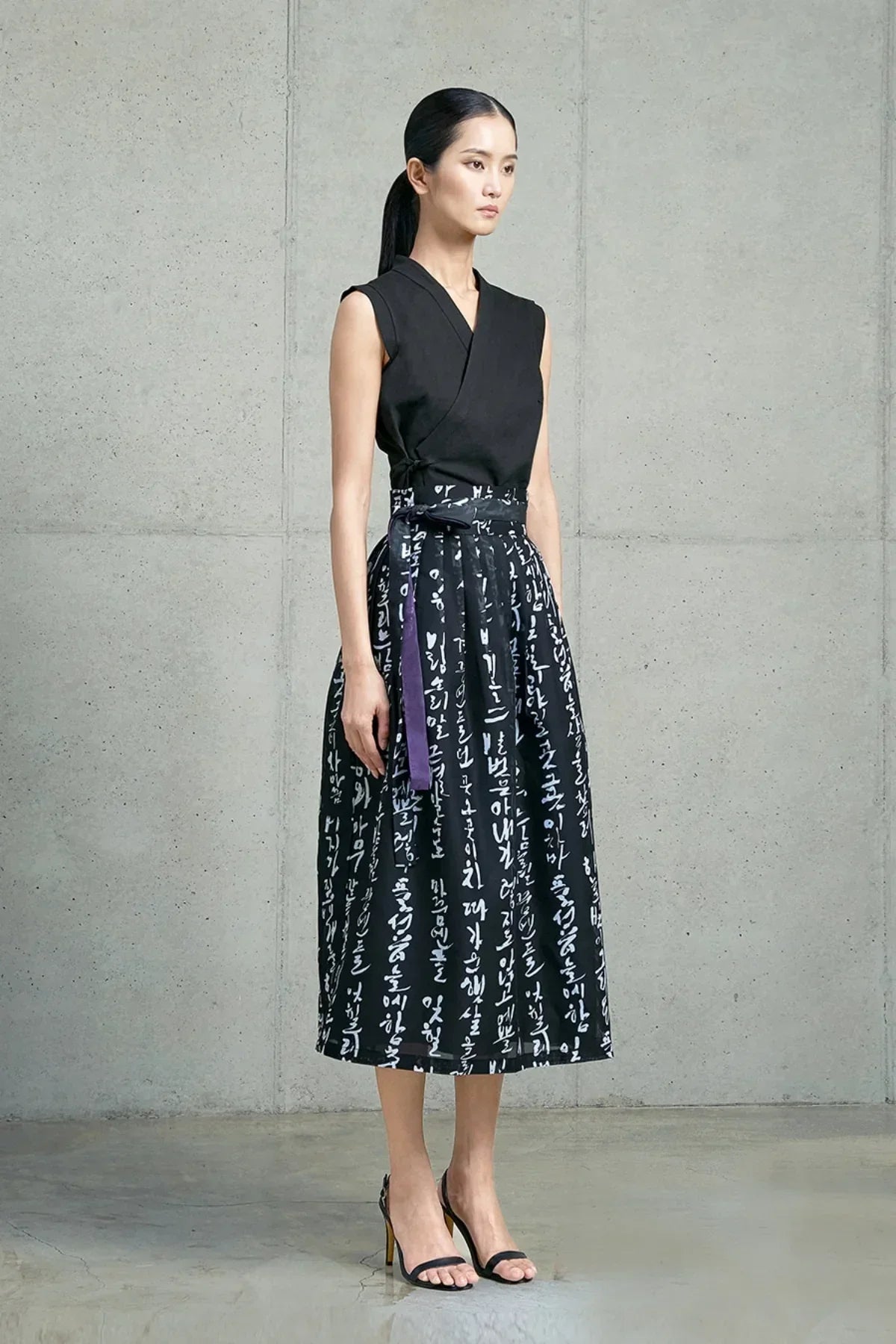 Woman wearing a black sleeveless top and a black skirt with white Hangeul characters, standing indoors