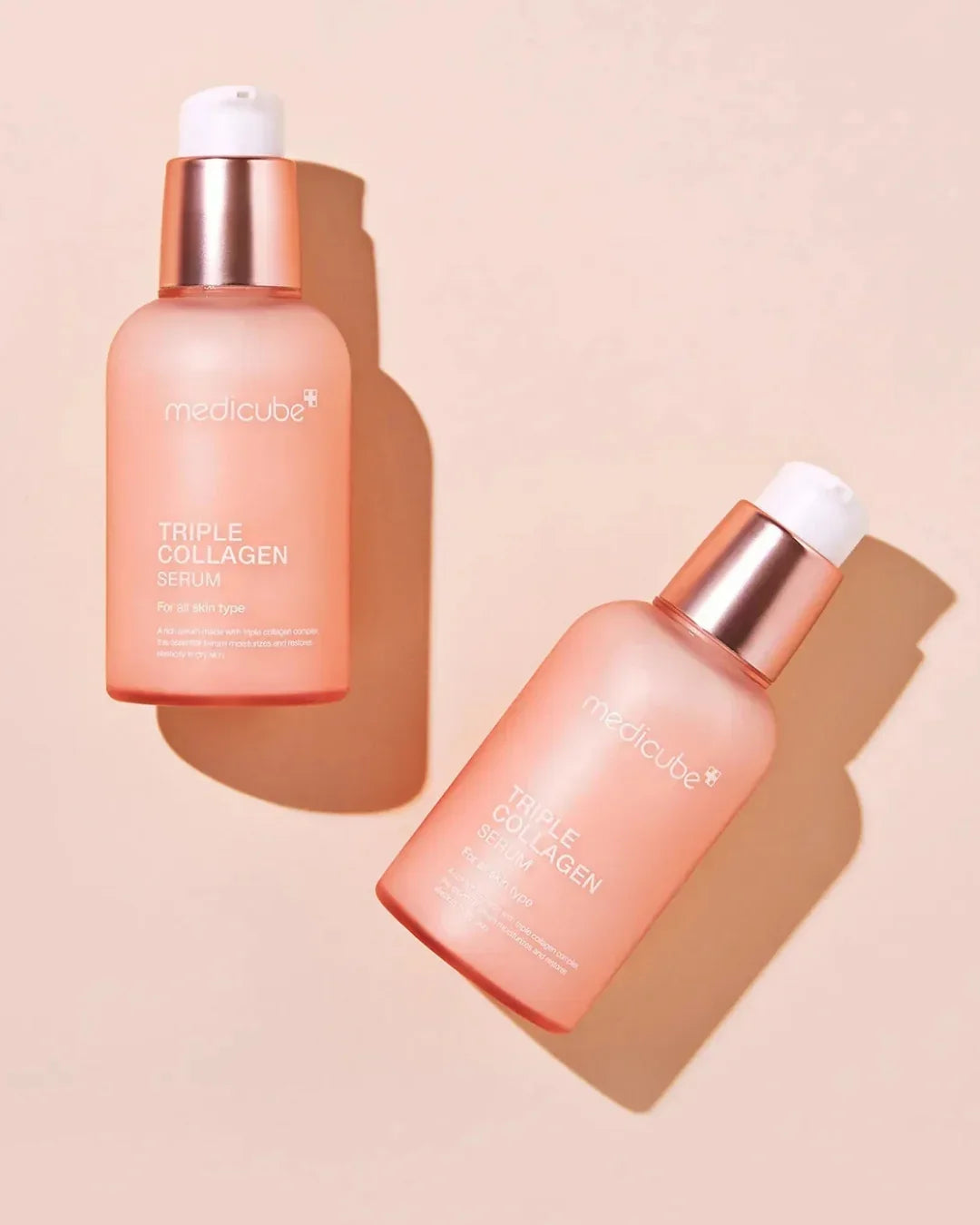 Two Medicube Triple Collagen Serum bottles with rose gold caps on peach background