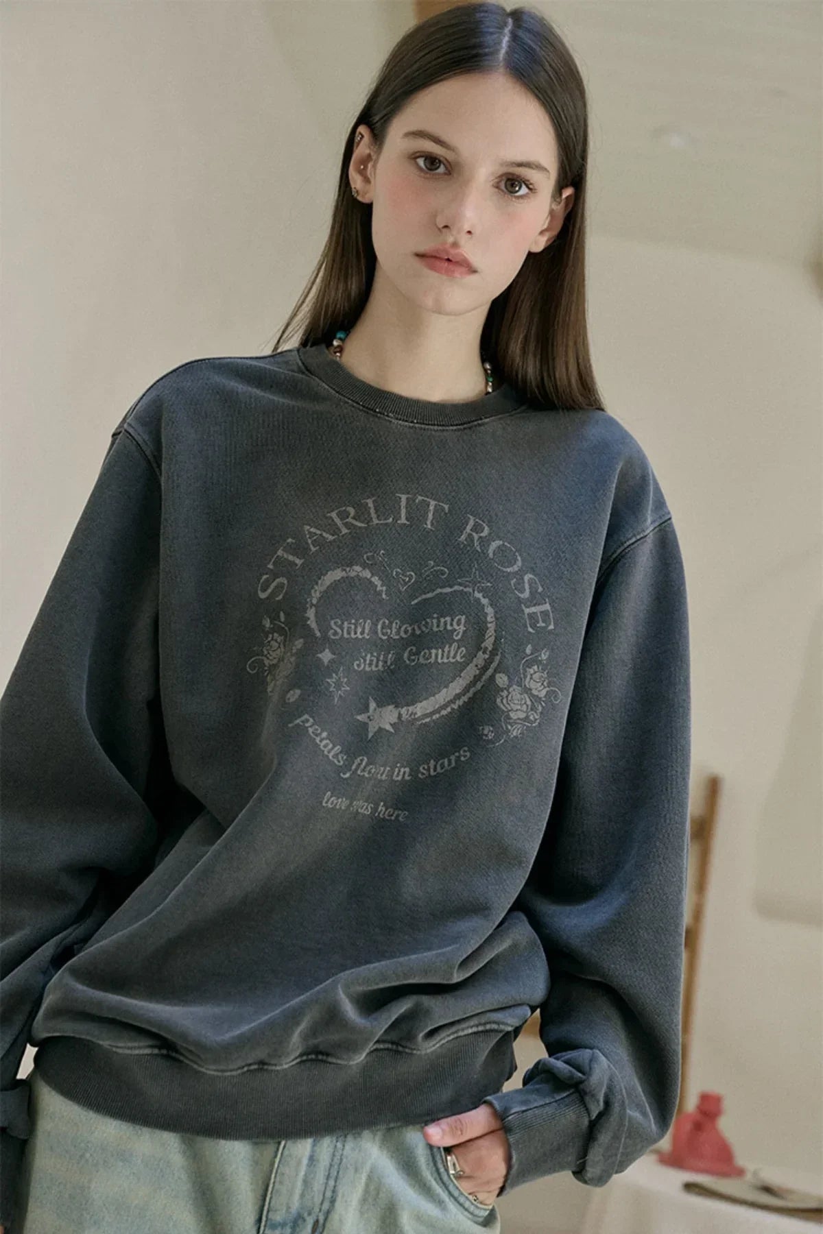 Young woman wearing a washed black Starlit Rose graphic sweatshirt with heart print indoors
