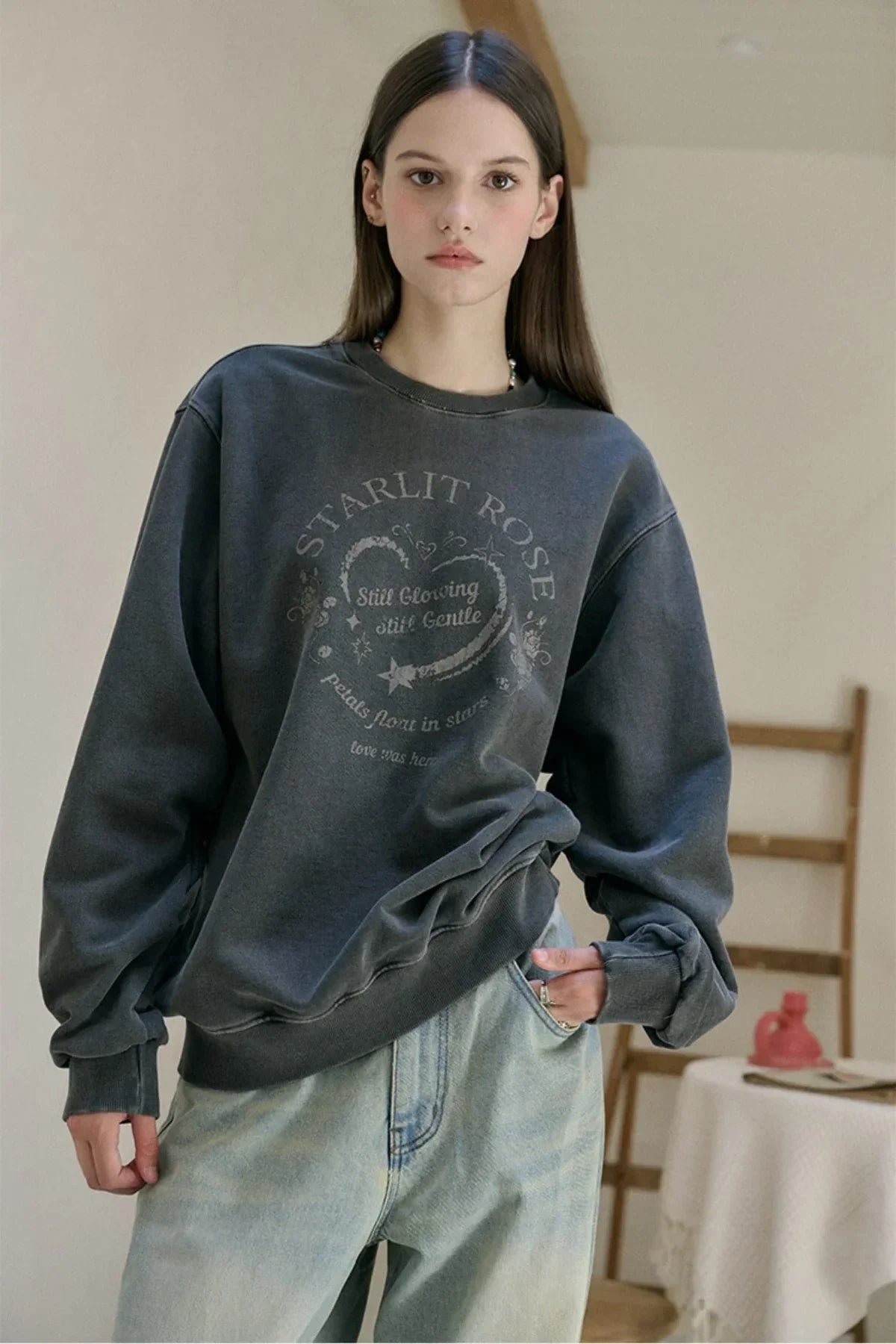 Young woman wearing a smoky black oversized sweatshirt with heart and text print, paired with light blue jeans indoors