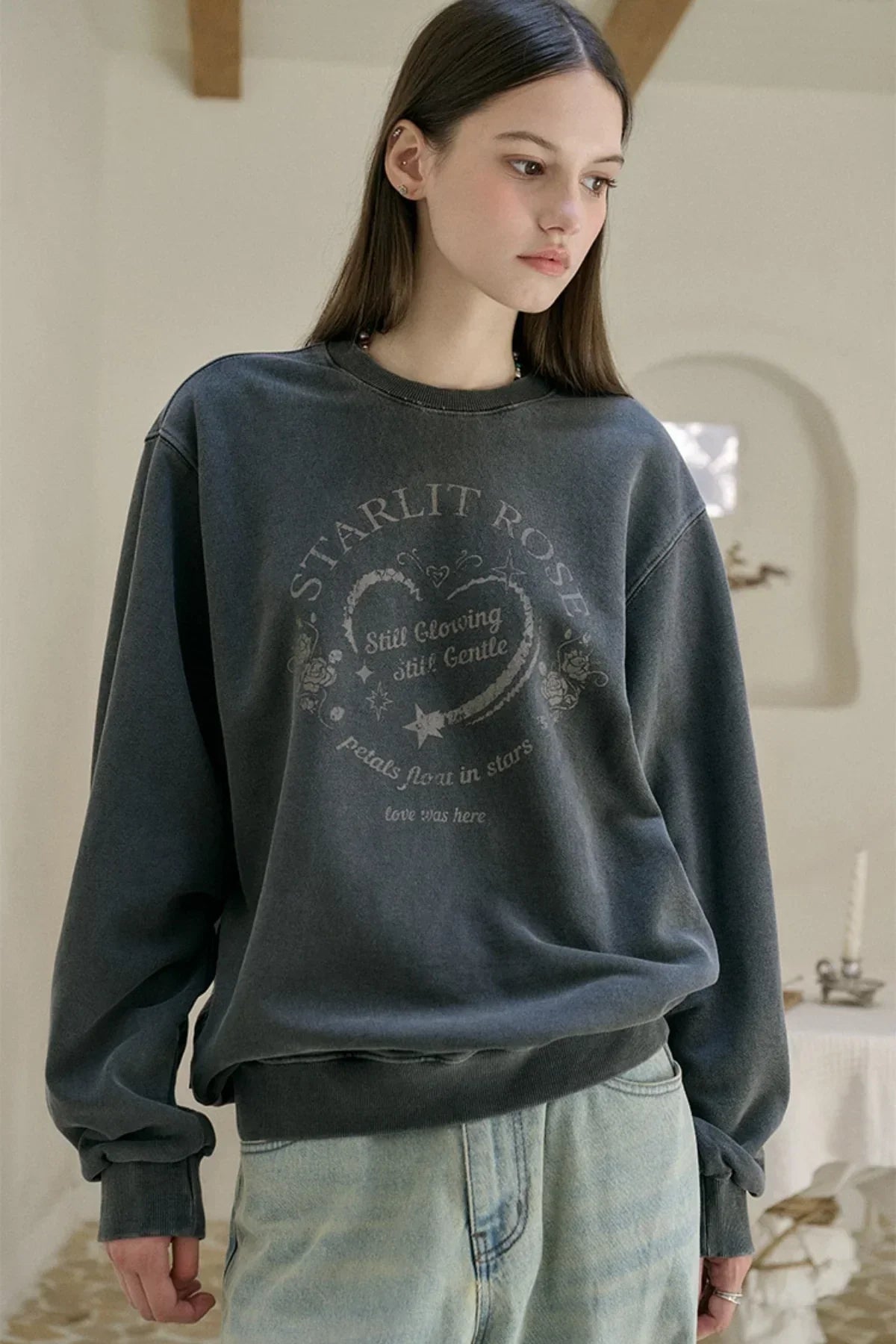 Young woman wearing smoke black oversized sweatshirt with heart and star graphic text in minimal indoor setting