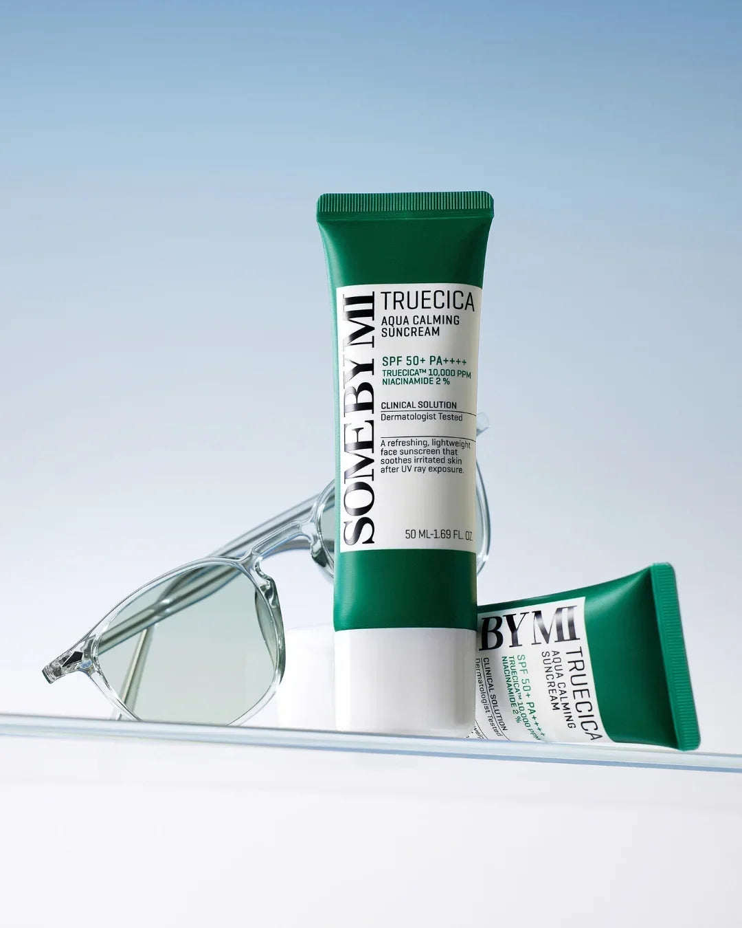 SOME BY MI Truecica Aqua Calming Suncream SPF 50+ tubes with clear sunglasses on reflective surface