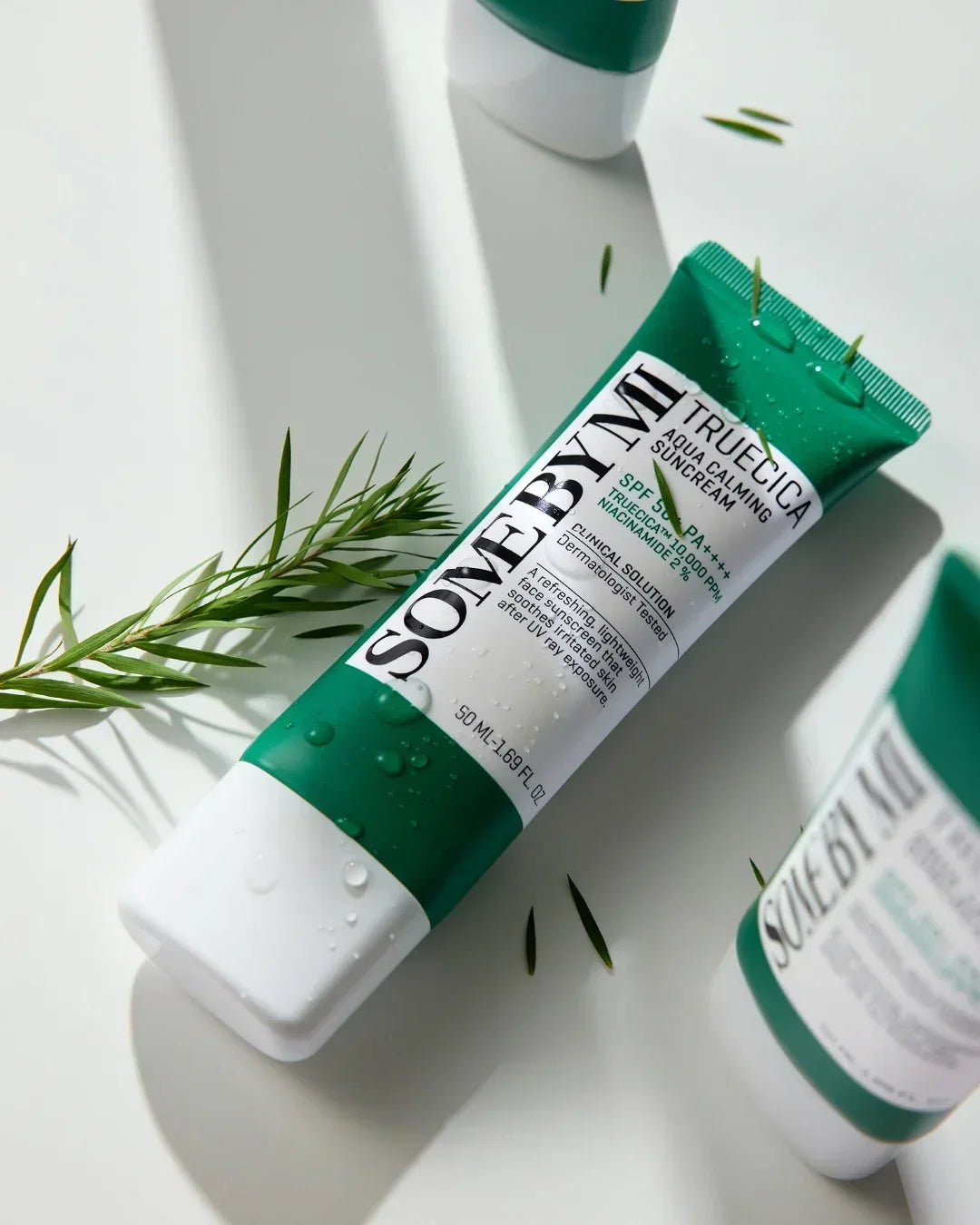 Tube of SOME BY MI Truecica Aqua Calming Suncream SPF 50+ PA++++ with water droplets and green plant leaves