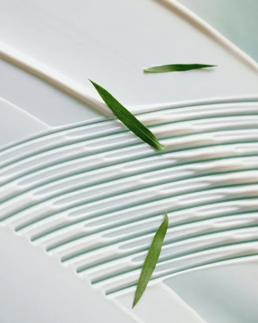 Close-up of white calming tone-up suncream texture with green leaves on a smooth surface