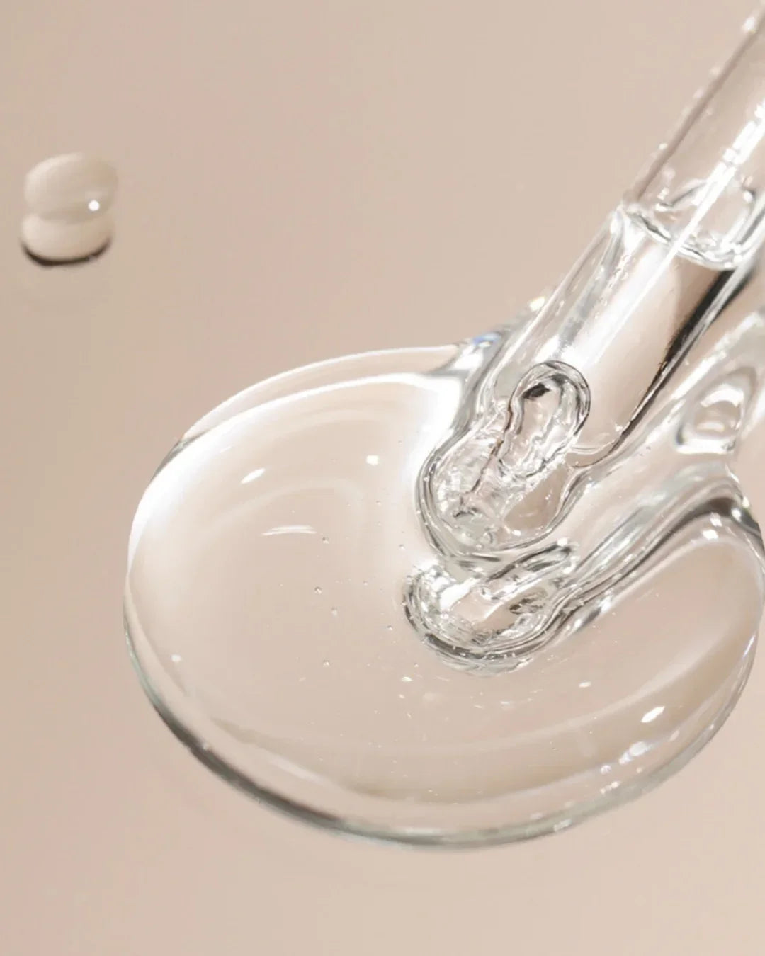 Close-up of clear serum drop with glass dropper on beige background, skincare product texture