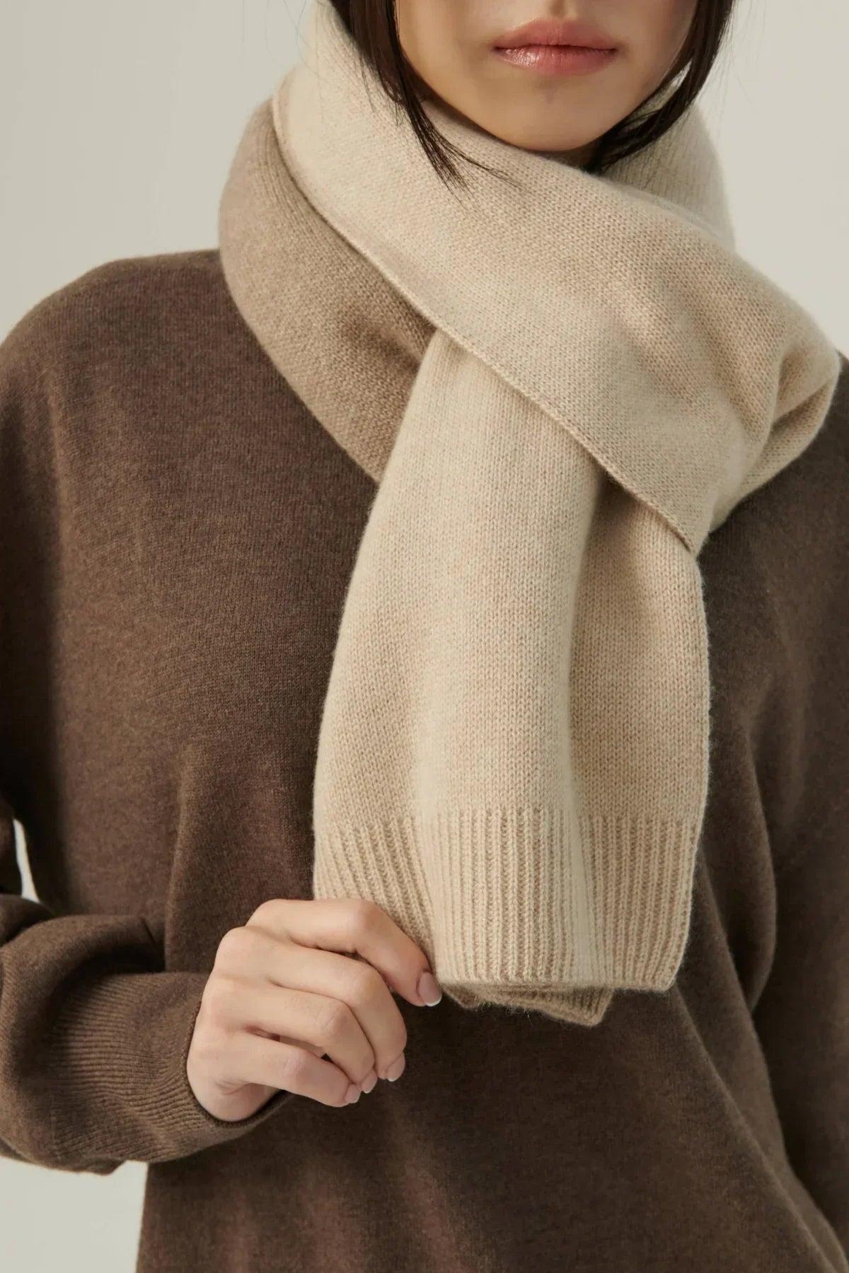 Close-up of a woman wearing a beige two-tone cashmere scarf over a brown sweater