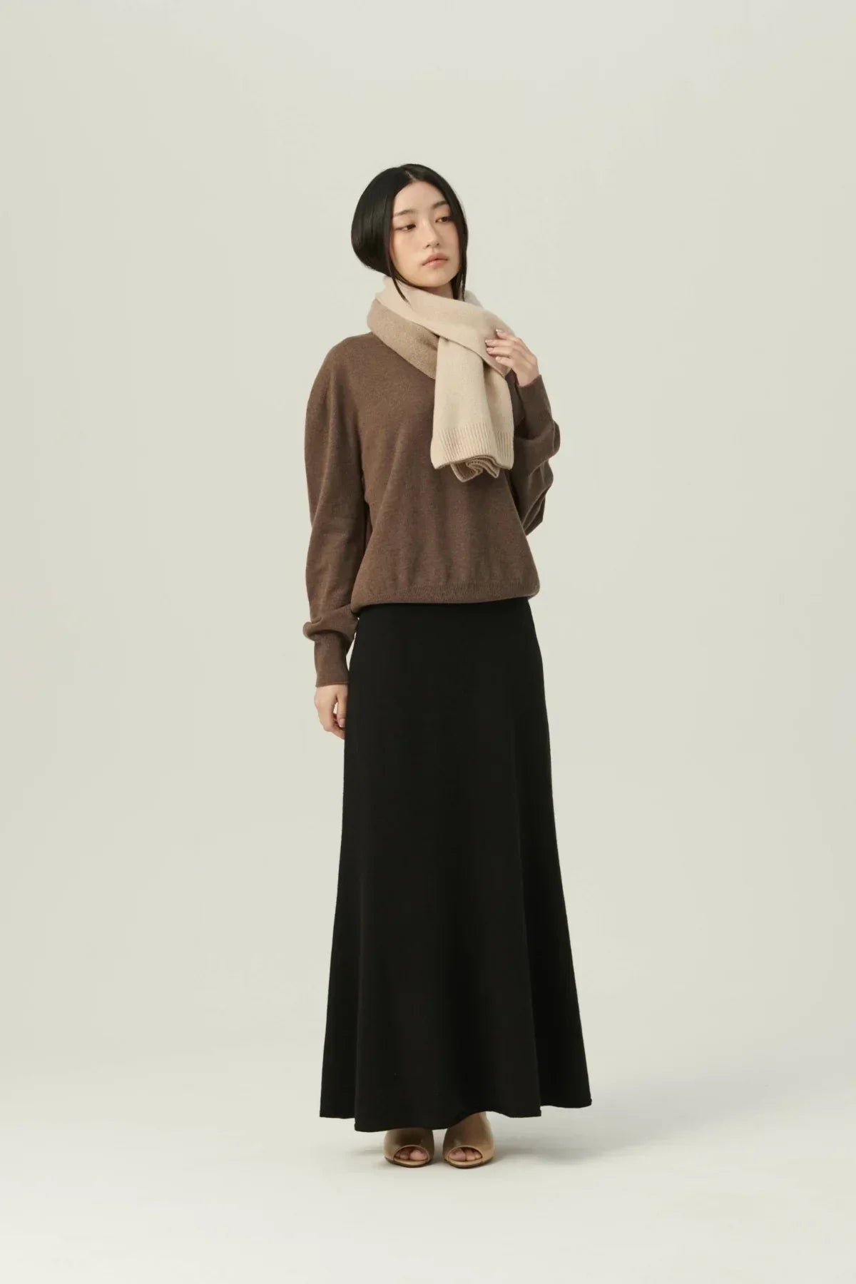 Woman wearing beige two-tone cashmere scarf with brown sweater, black maxi skirt, and beige heels