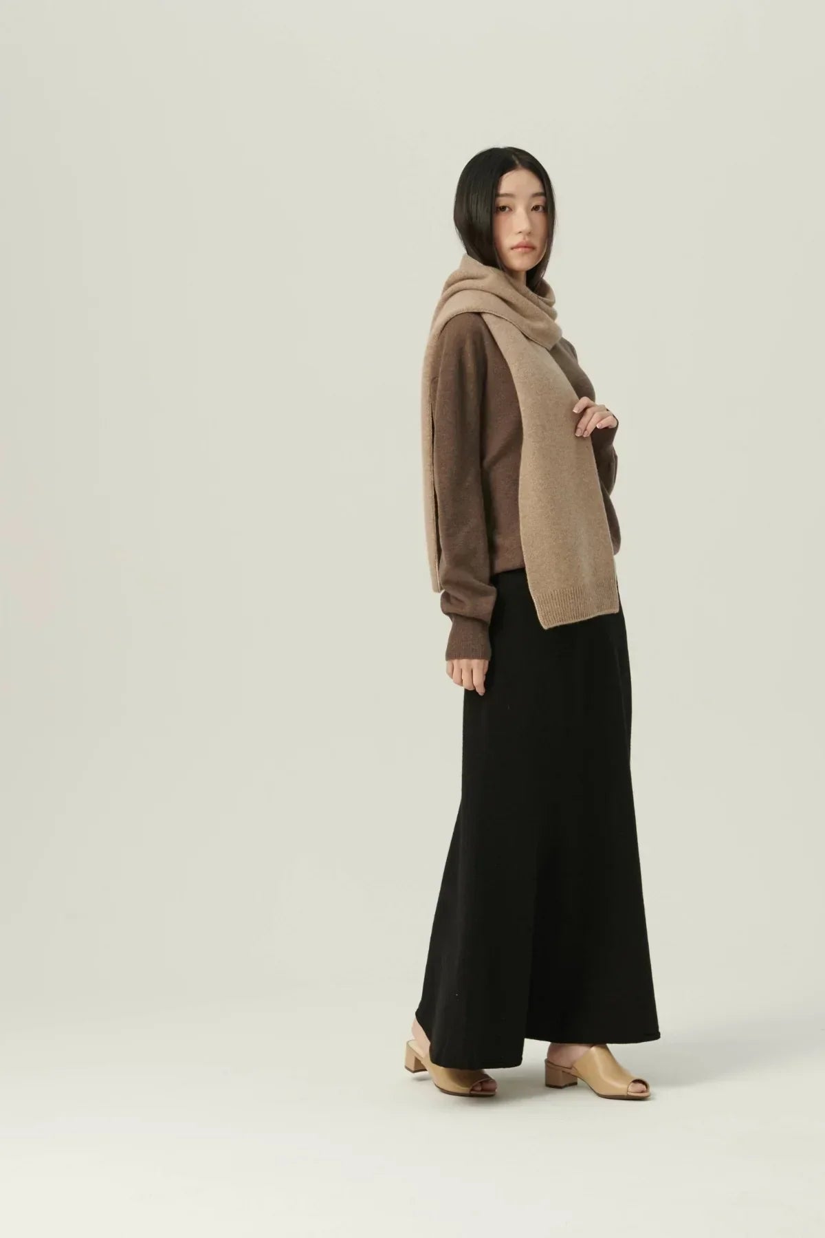 Asian woman wearing beige two-tone cashmere muffler with brown sweater, black skirt, and beige sandals