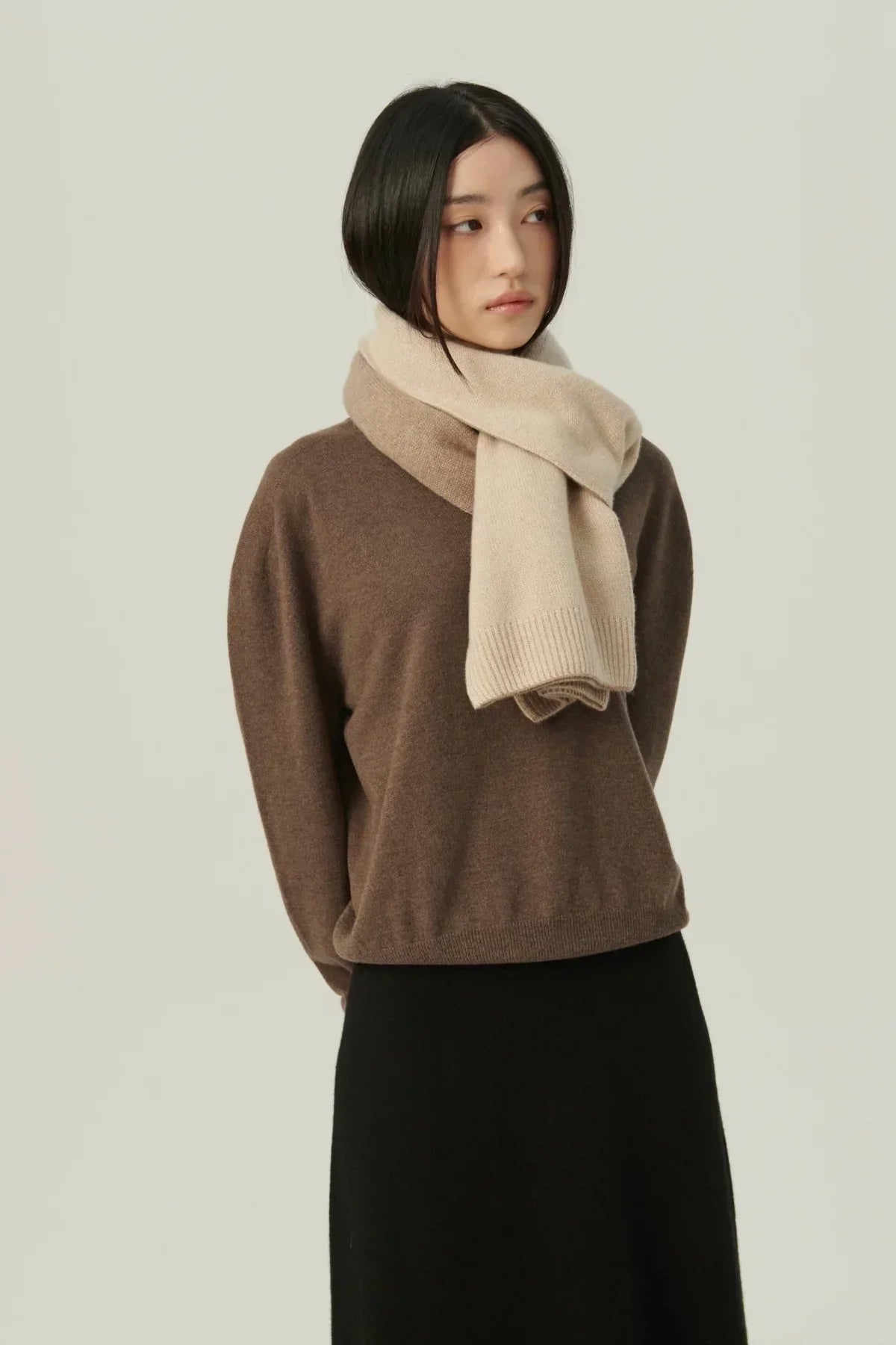 Woman wearing two-tone beige and brown cashmere scarf with brown sweater and black skirt