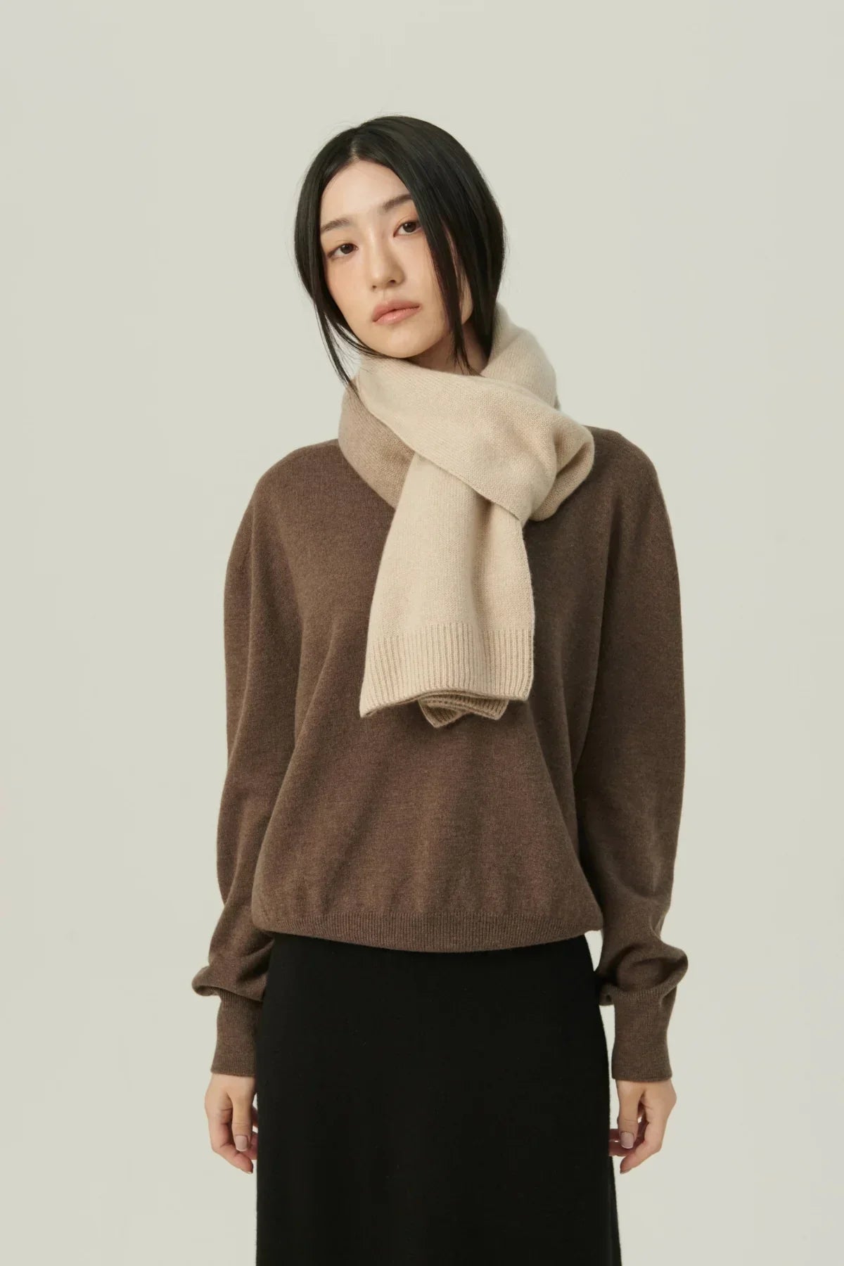 Woman wearing two-tone beige cashmere scarf over brown sweater and black skirt on neutral background