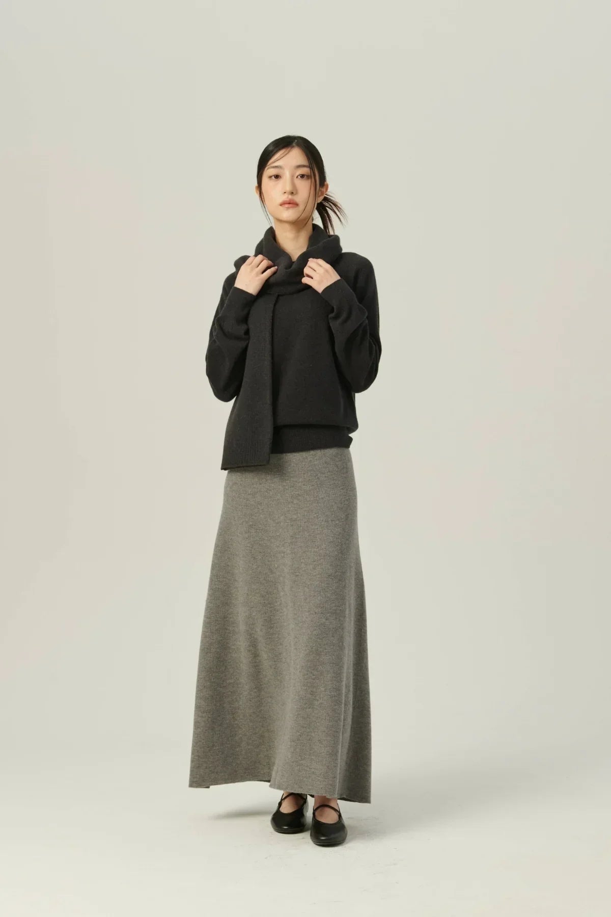 Woman wearing black cashmere sweater with mask and long gray knit skirt on light background