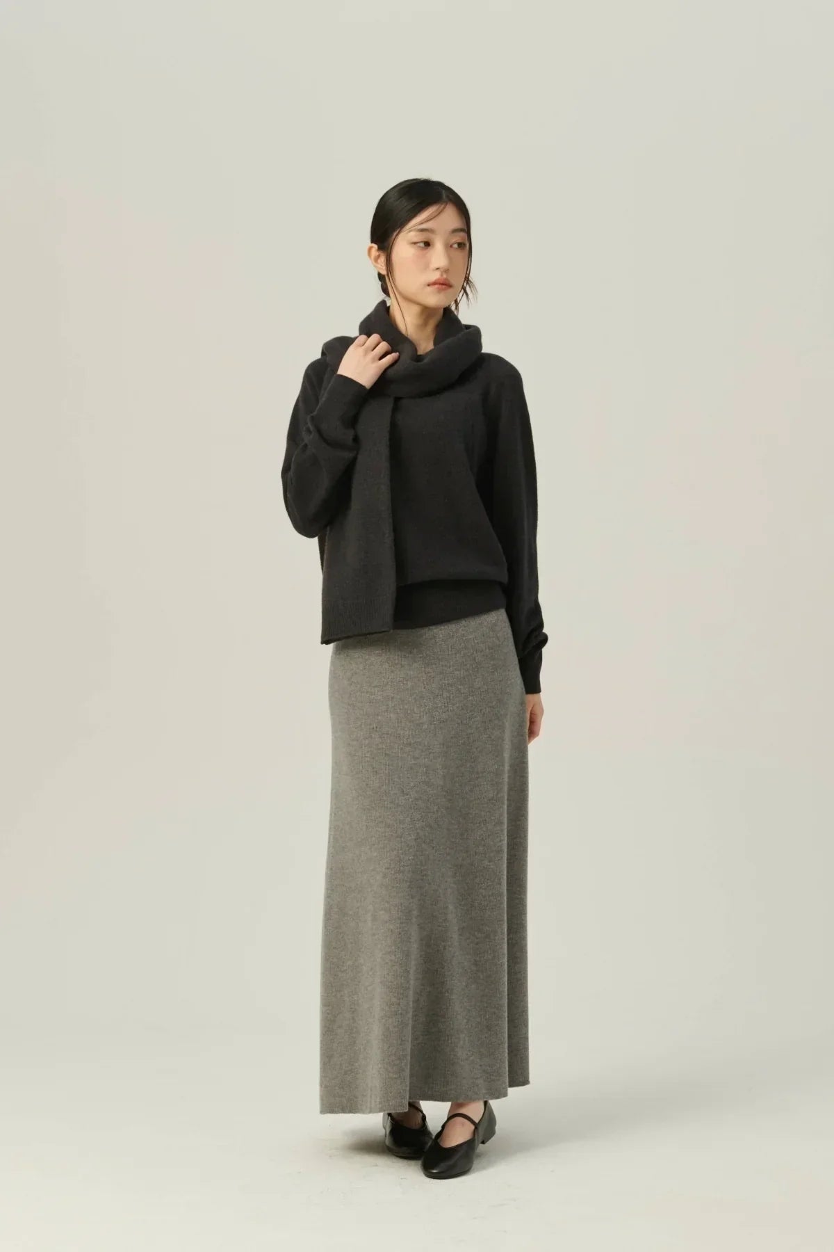 Woman wearing black cashmere sweater and scarf with long gray knit skirt and black shoes