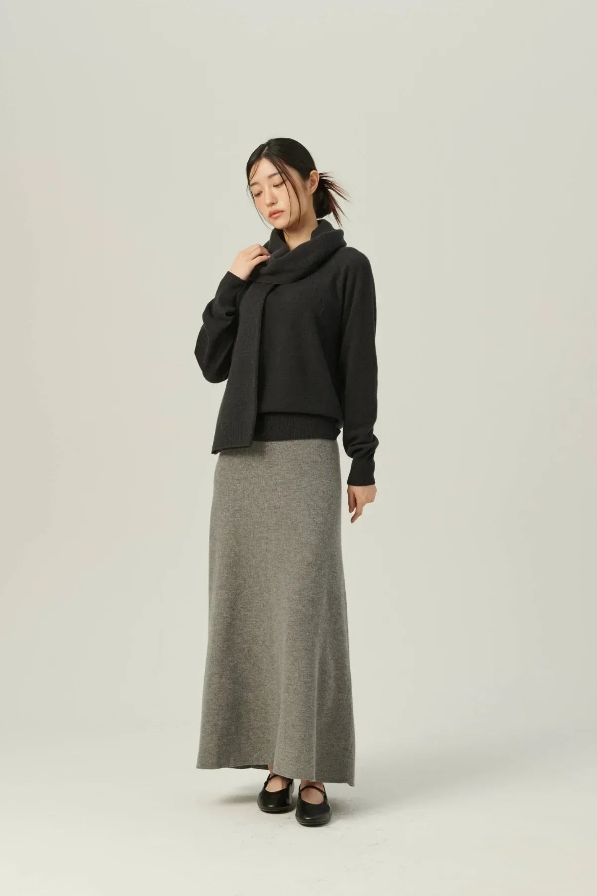 Woman wearing a black cashmere scarf and sweater with a long gray skirt and black flats