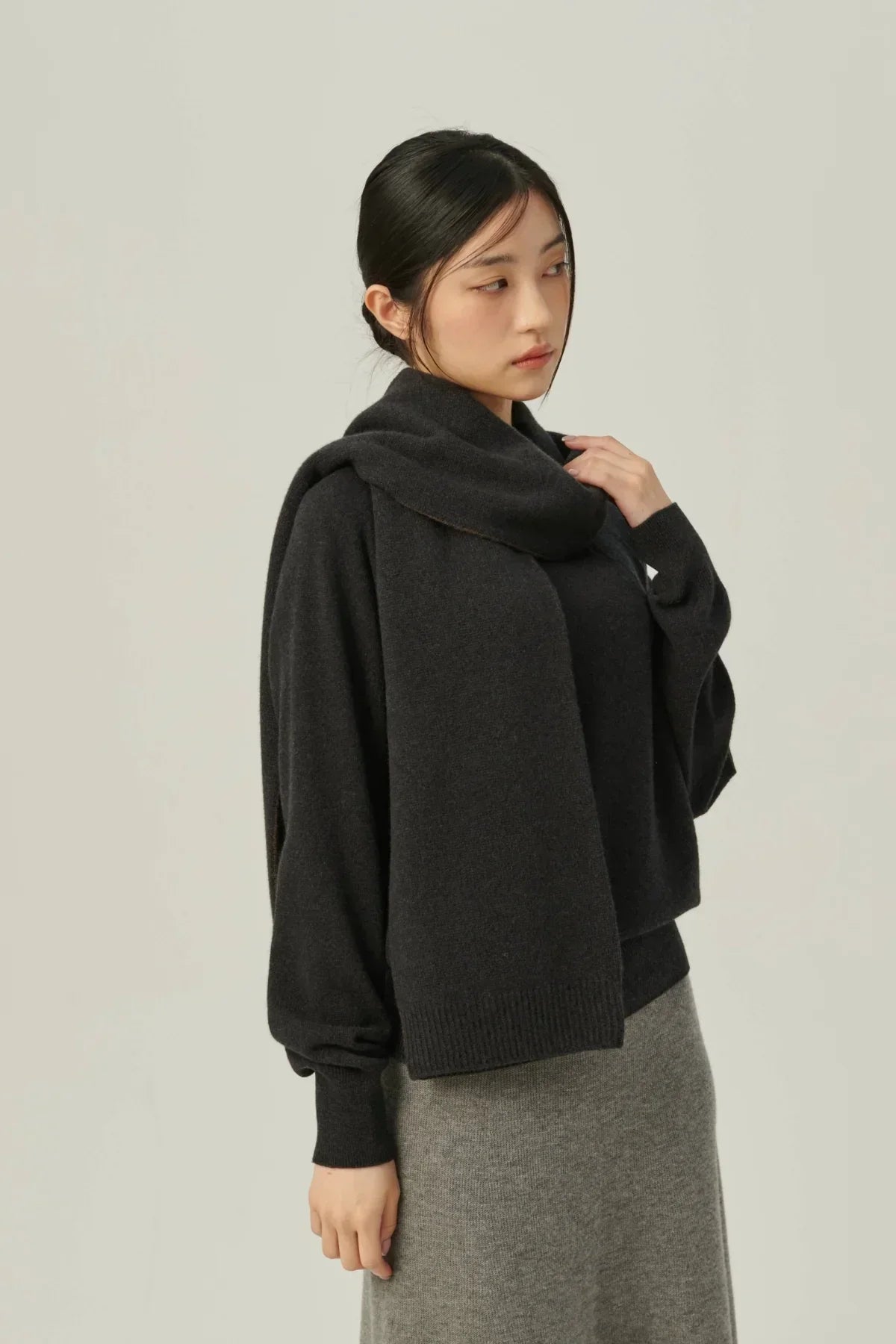 Woman wearing dark charcoal cashmere sweater with matching scarf and gray knit skirt on beige background