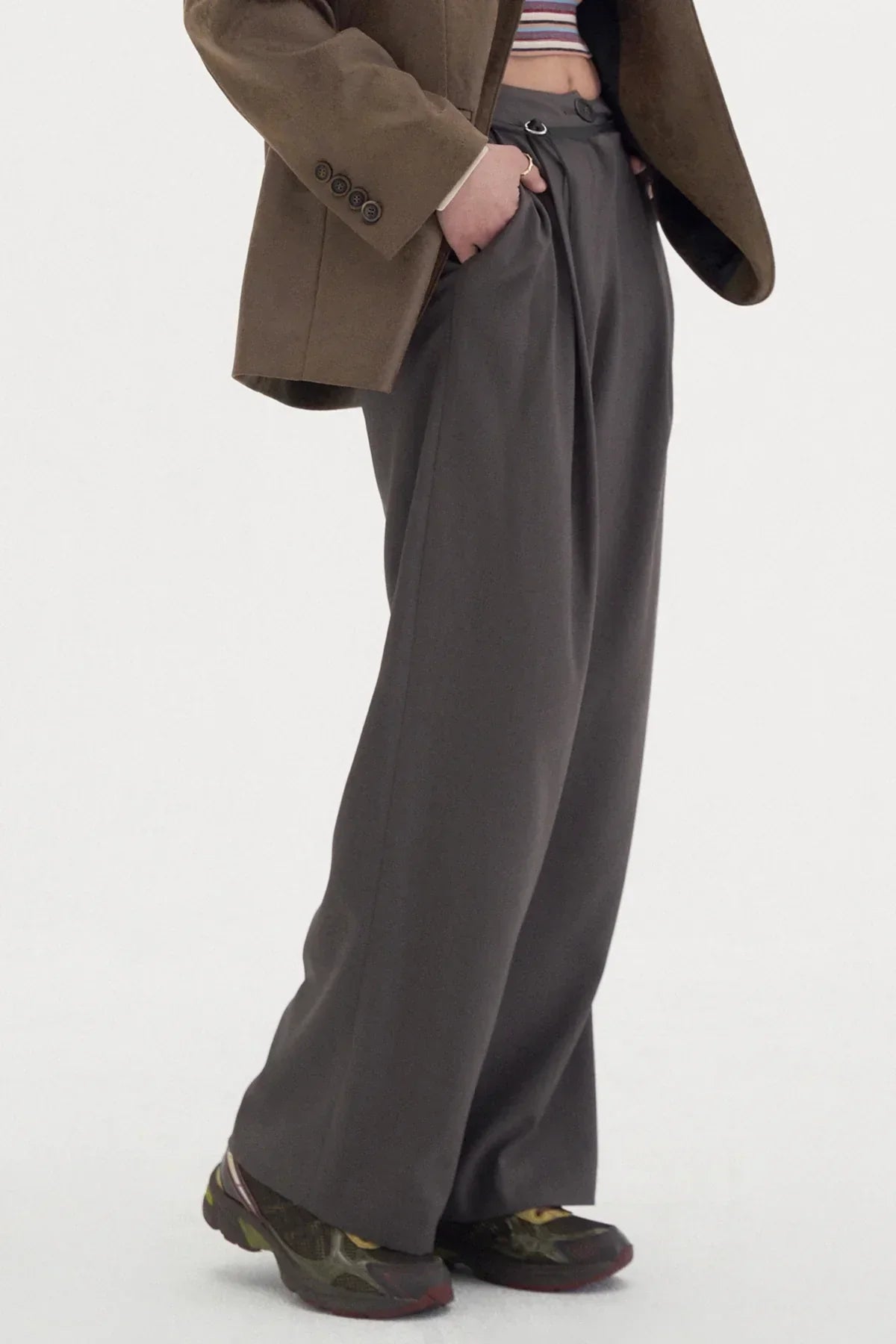Close-up of wide-leg gray slacks with two tucks, paired with brown jacket and black sneakers