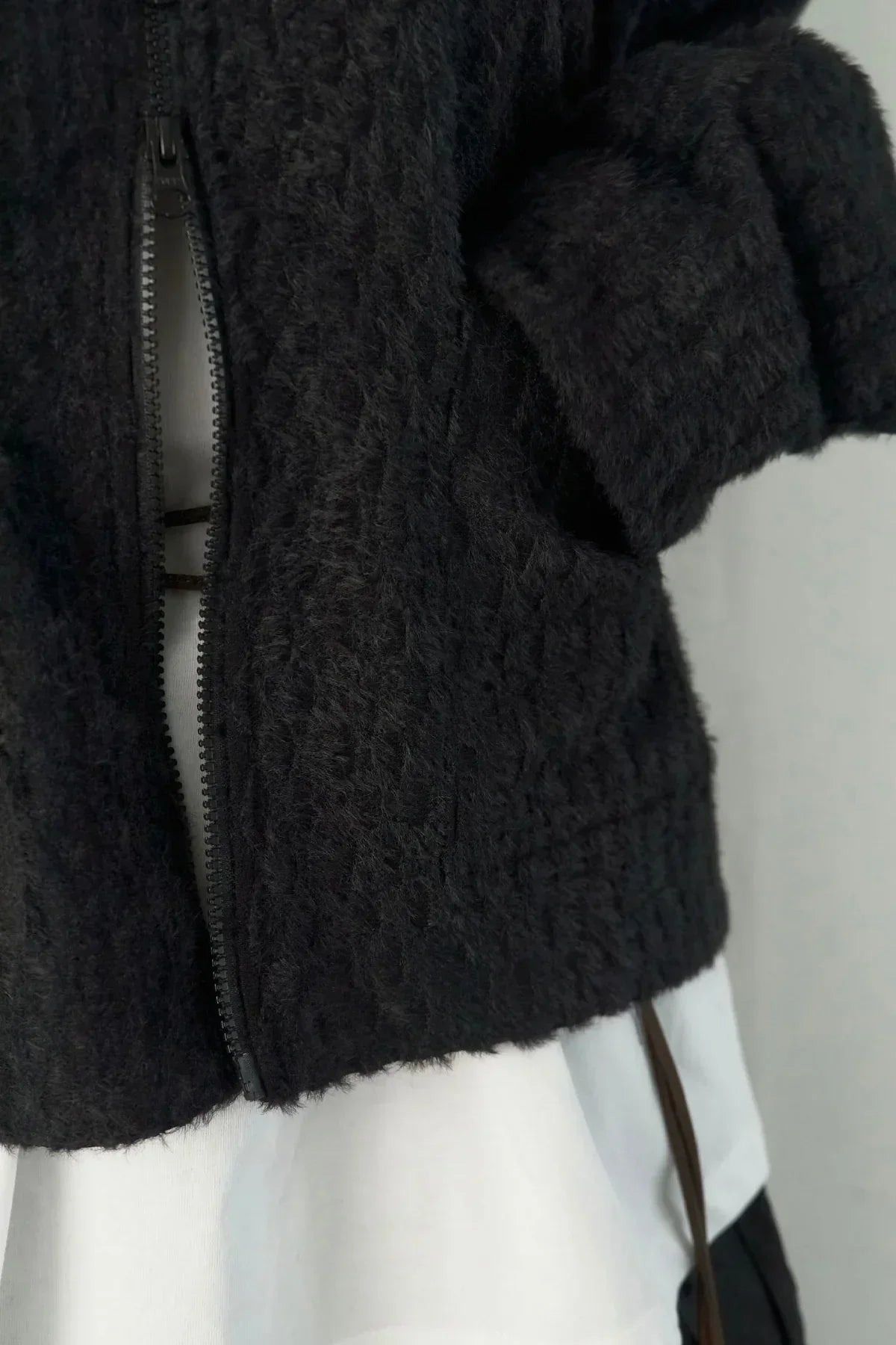 Close-up of black textured knit jacket with zipper over white garment