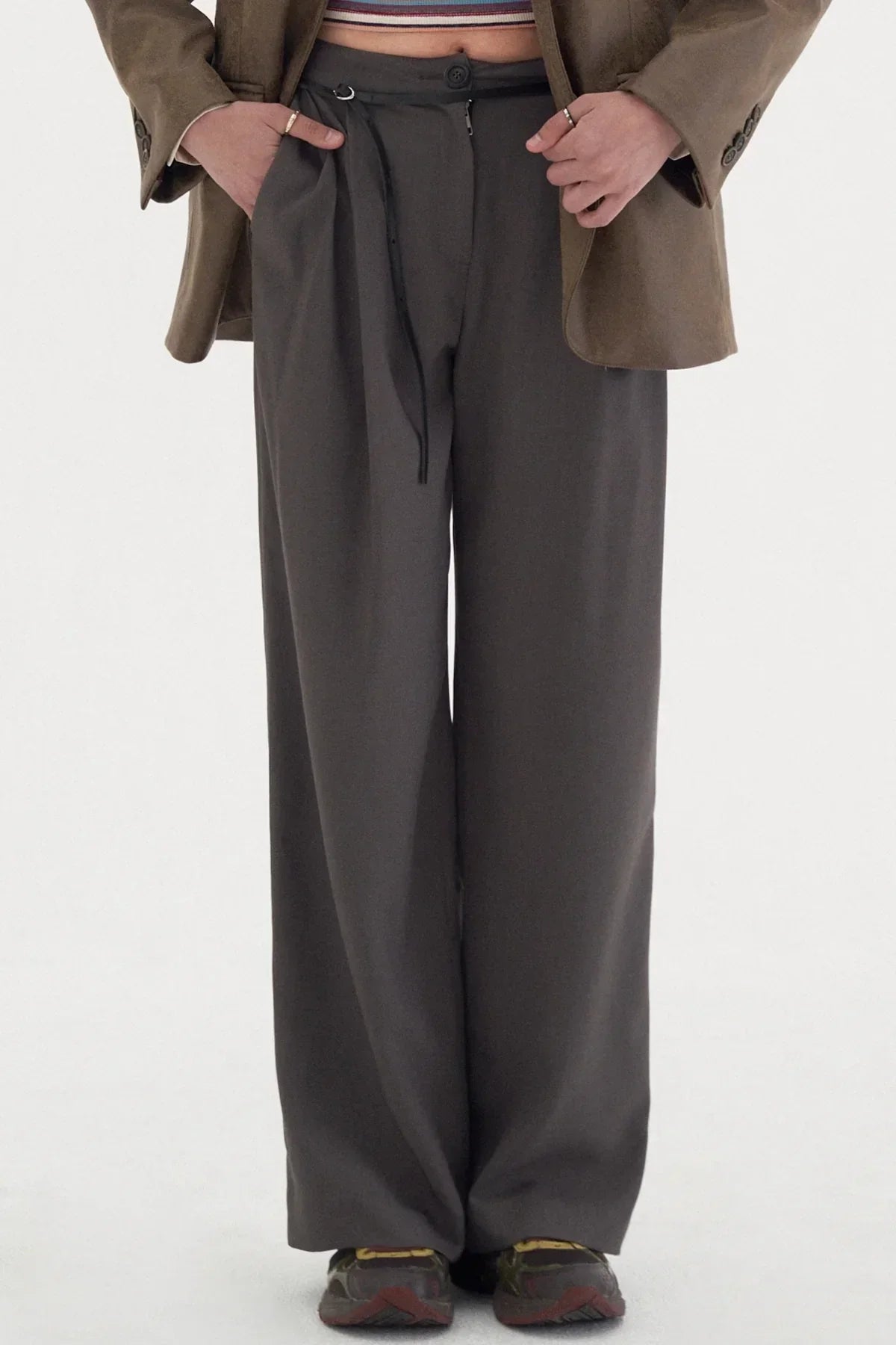 Person wearing dark wide-leg two-tuck slacks with a brown blazer and sneakers in studio