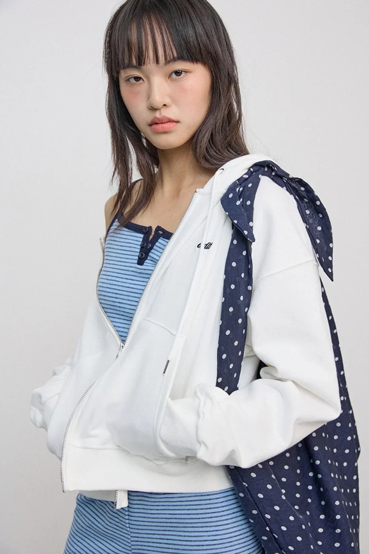 Young woman wearing ivory zip-up hoodie over blue striped tank top with navy polka dot tote bag