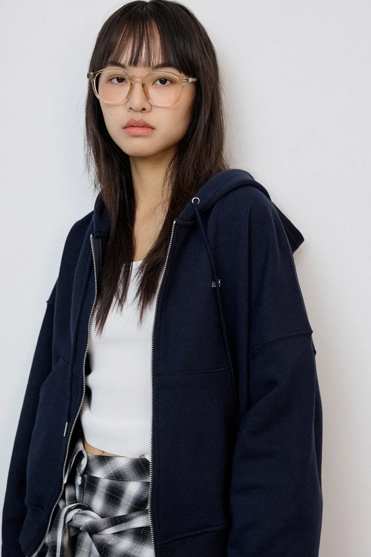 Young woman wearing navy zip-up hoodie, white tank top, and plaid shirt tied at waist