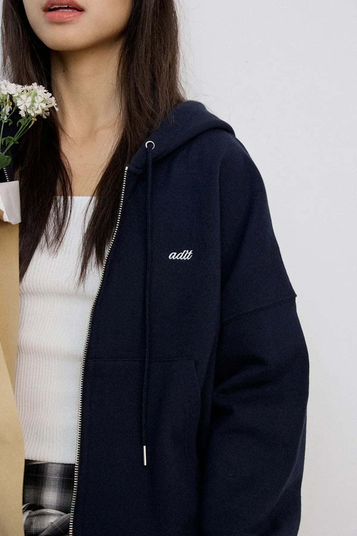 Close-up of woman wearing navy blue zip-up hoodie with white adit logo and holding flowers