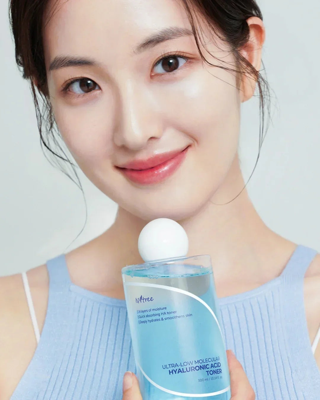 Young woman with glowing skin holding a 300ml bottle of ultra-low molecular hyaluronic acid toner