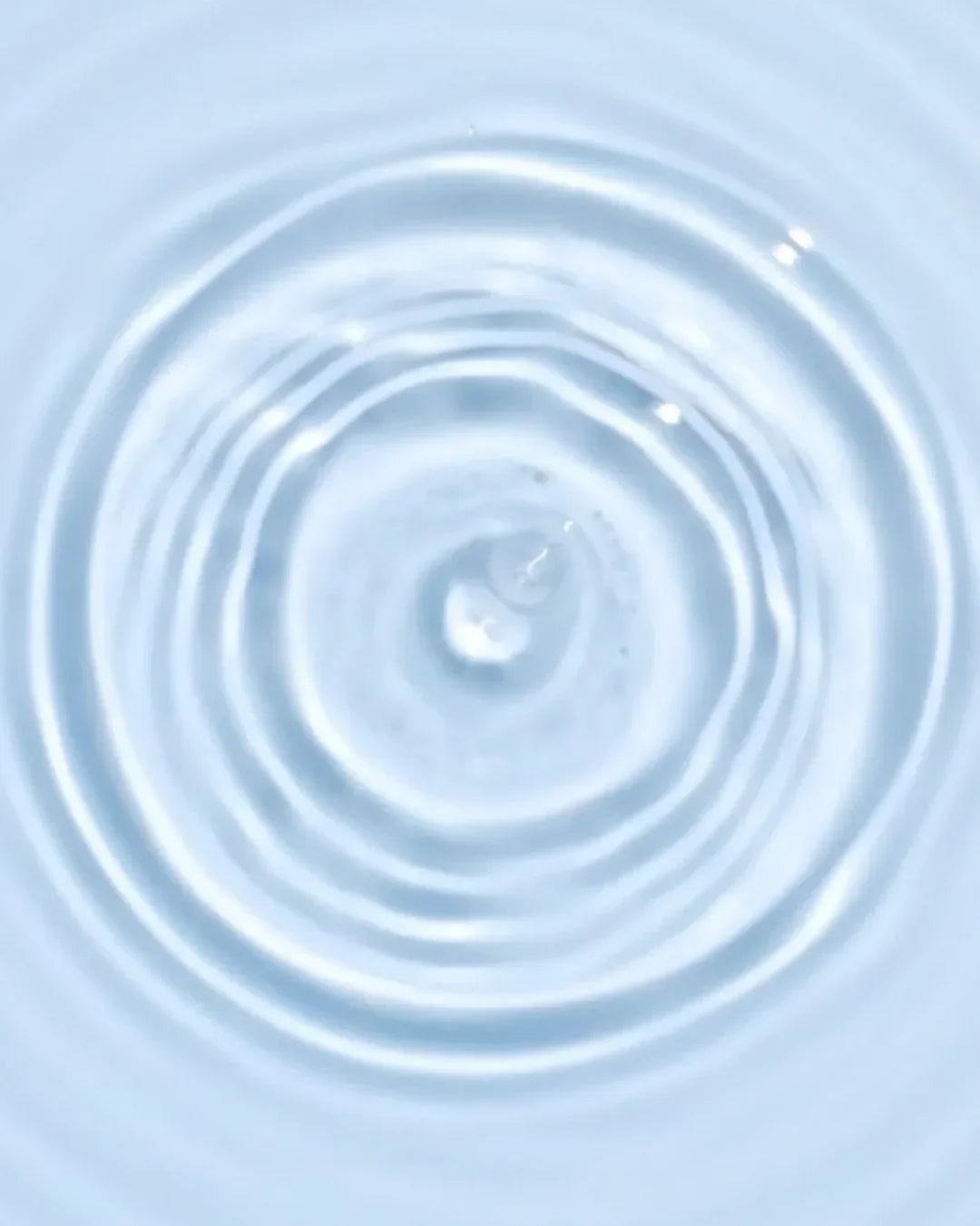Close-up of clear water droplet creating ripples in light blue liquid texture