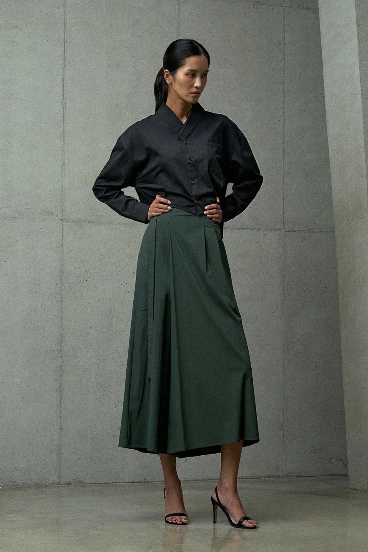 woman in black blouse and dark green midi skirt posing in minimalistic concrete interior