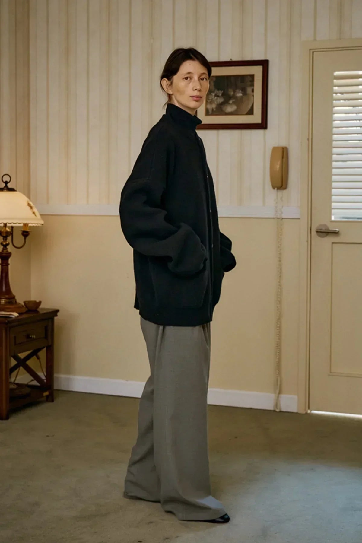 Person wearing a black unisex cashmere cardigan with gray wide-leg trousers in a cozy room