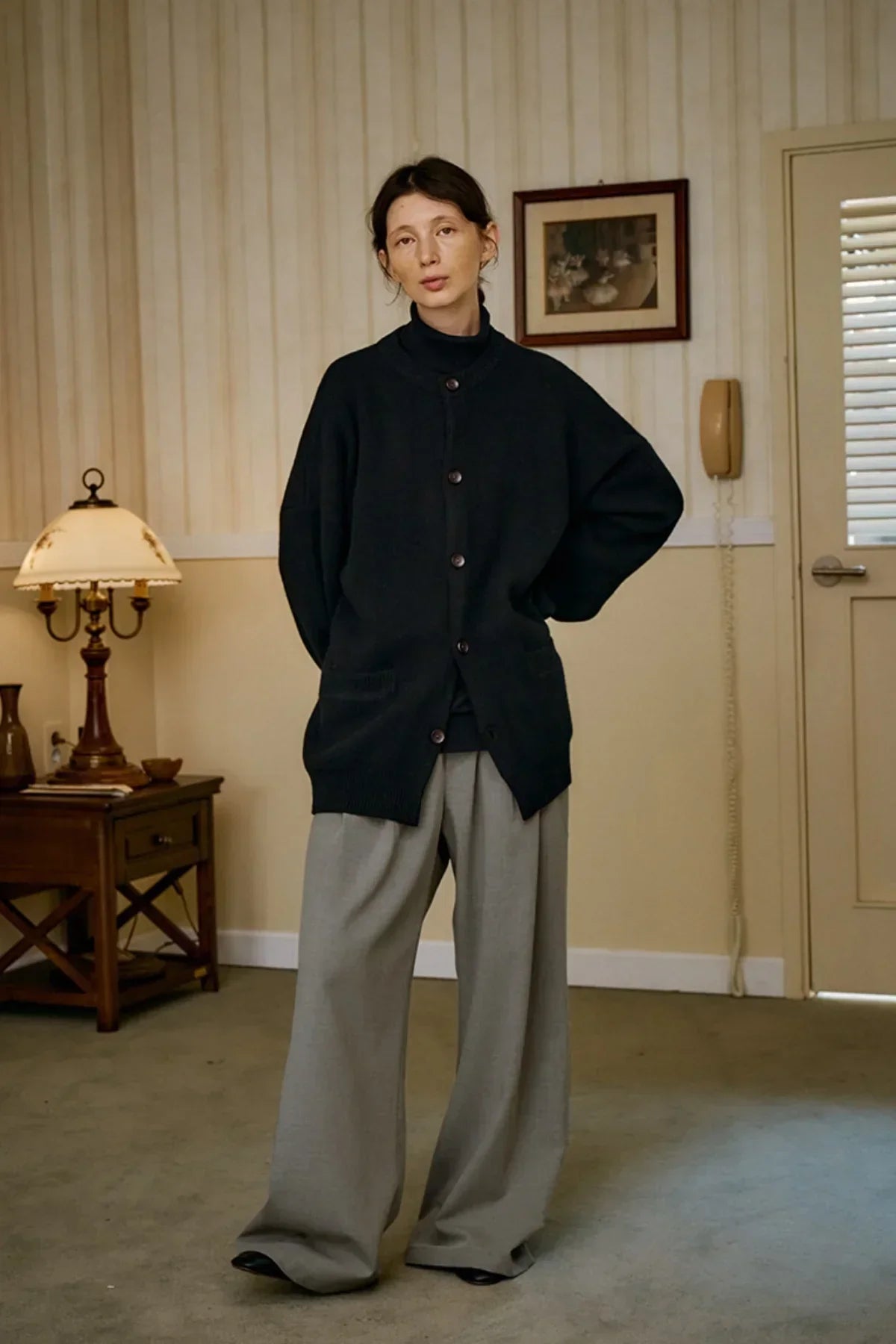 Model wearing black unisex cashmere cardigan and wide gray trousers in vintage room setting