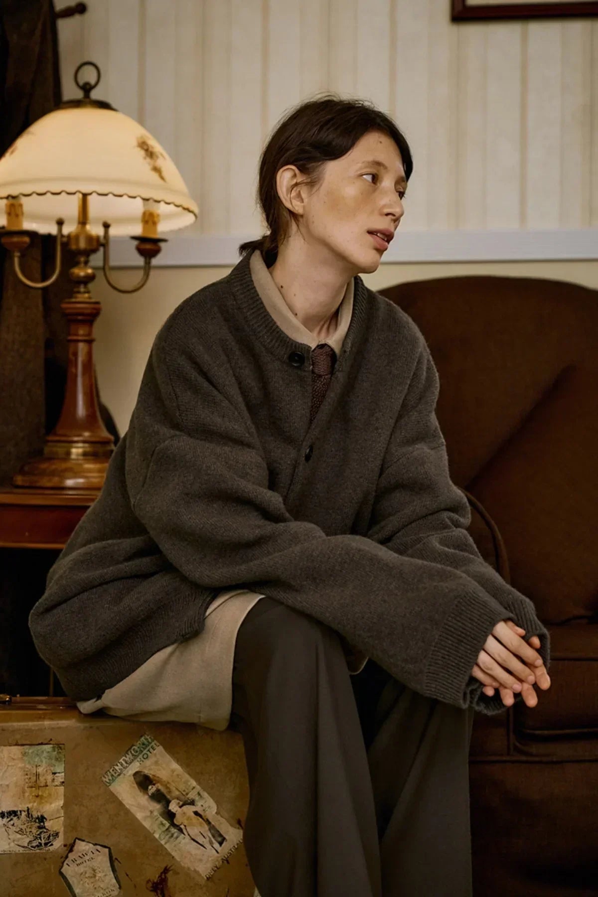 Person wearing oversized dark brown cashmere cardigan sitting indoors on vintage trunk